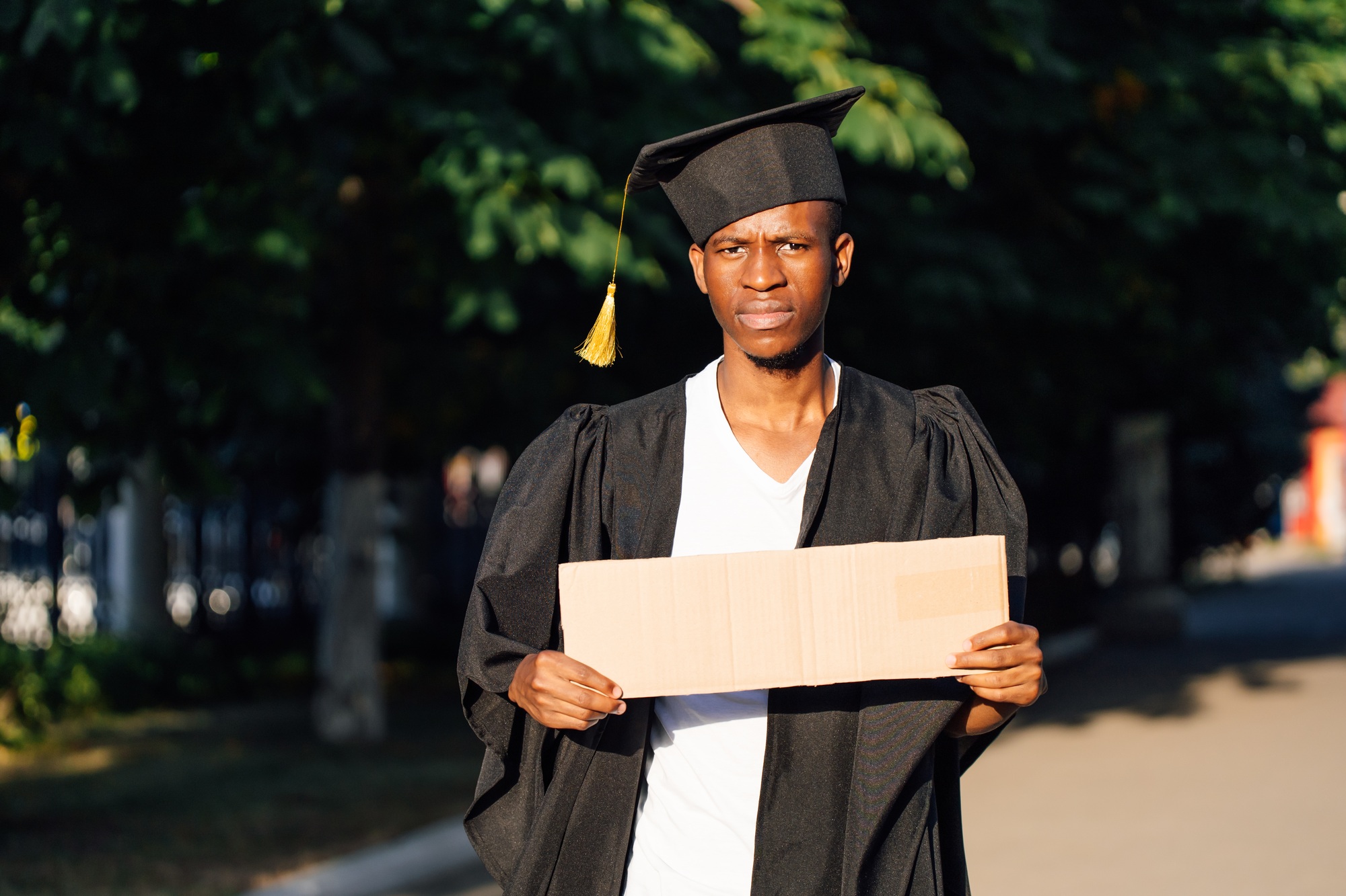 Portrait of rejoicing black guy standing with empty cardboard poster on street in sunny day looking