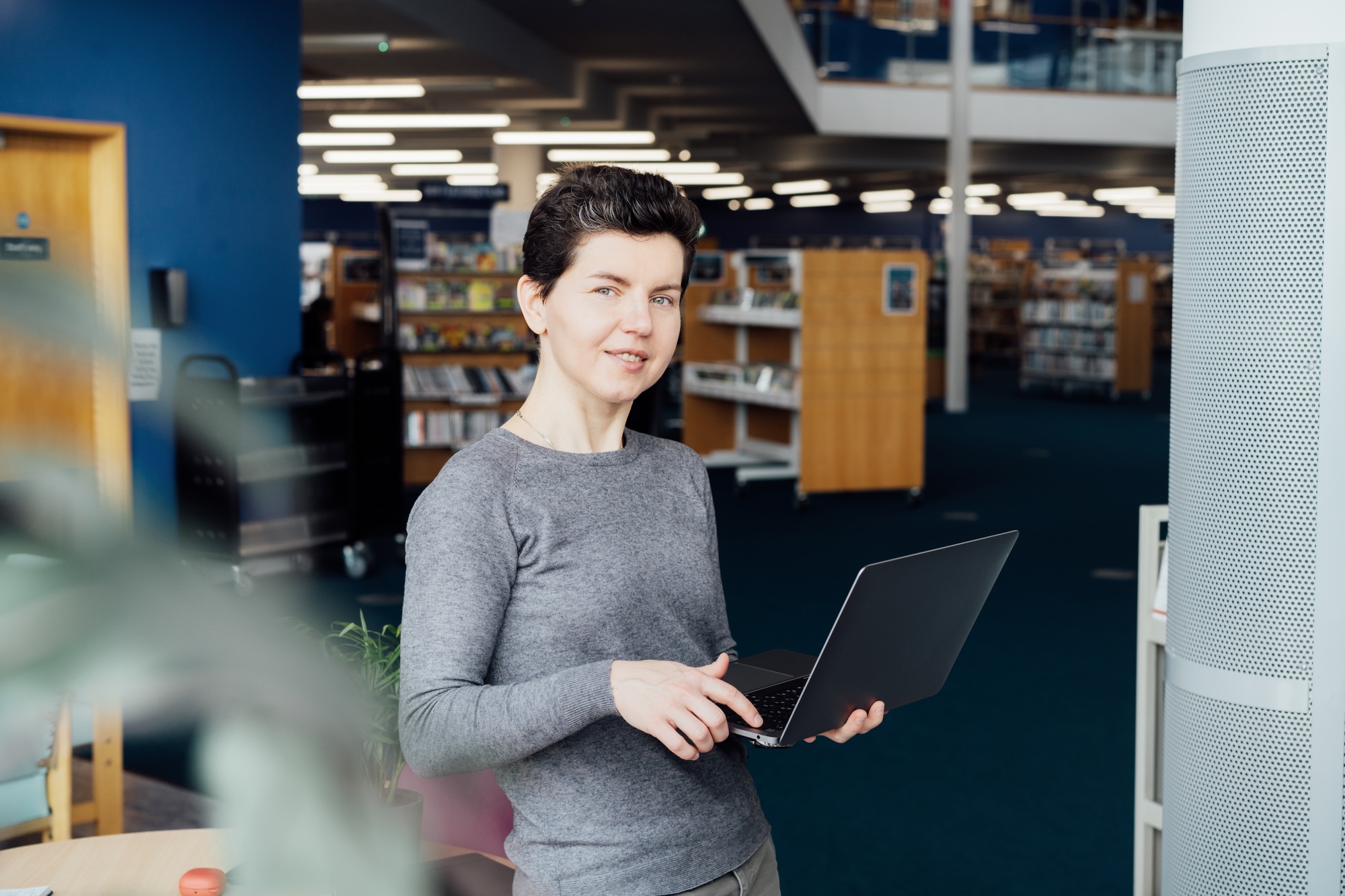 Portrait of Smiling neutral gender middleaged female person taking note on laptop working in library