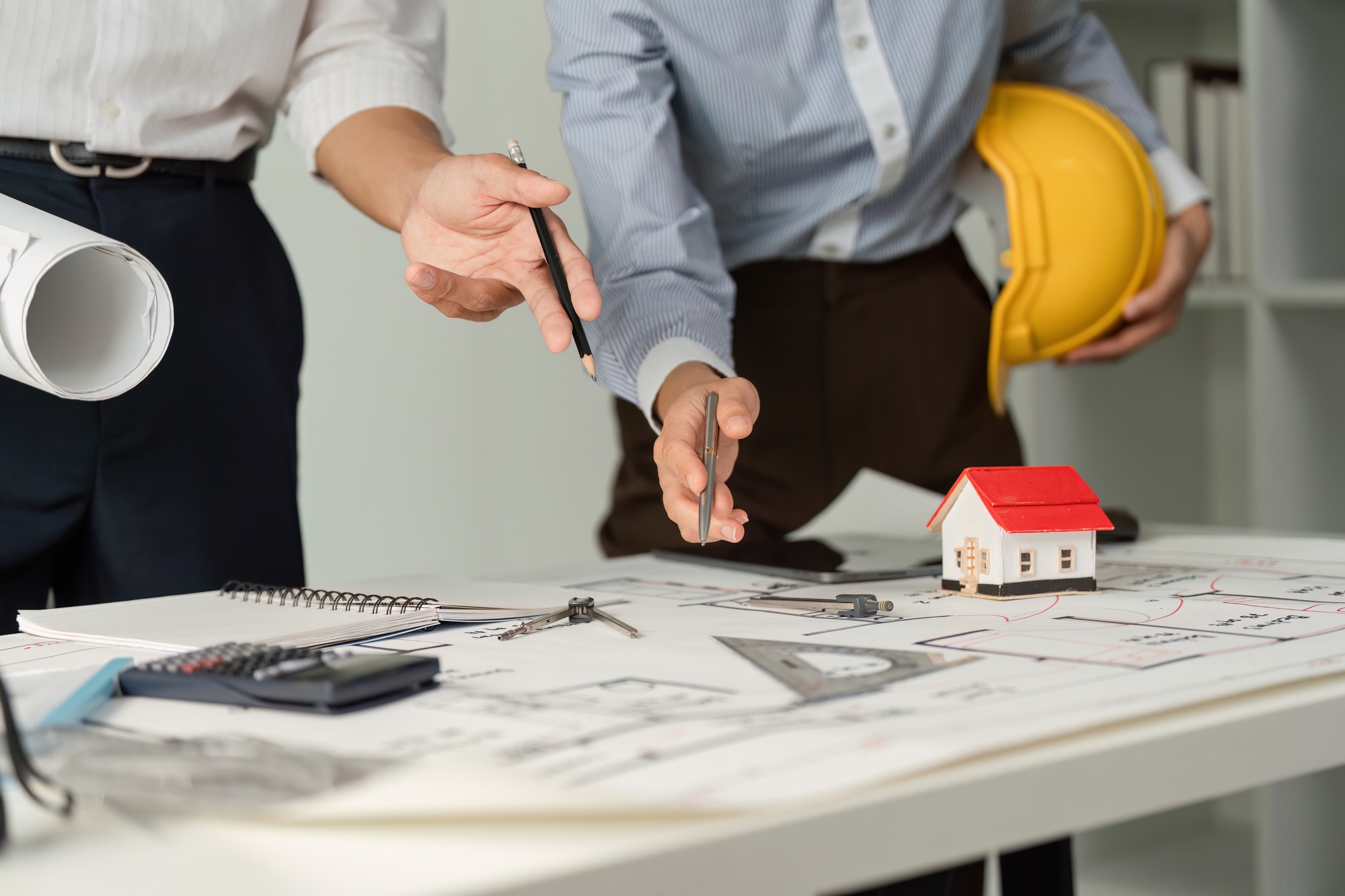 Professionals strategizing over architectural designs with tools and a model house.