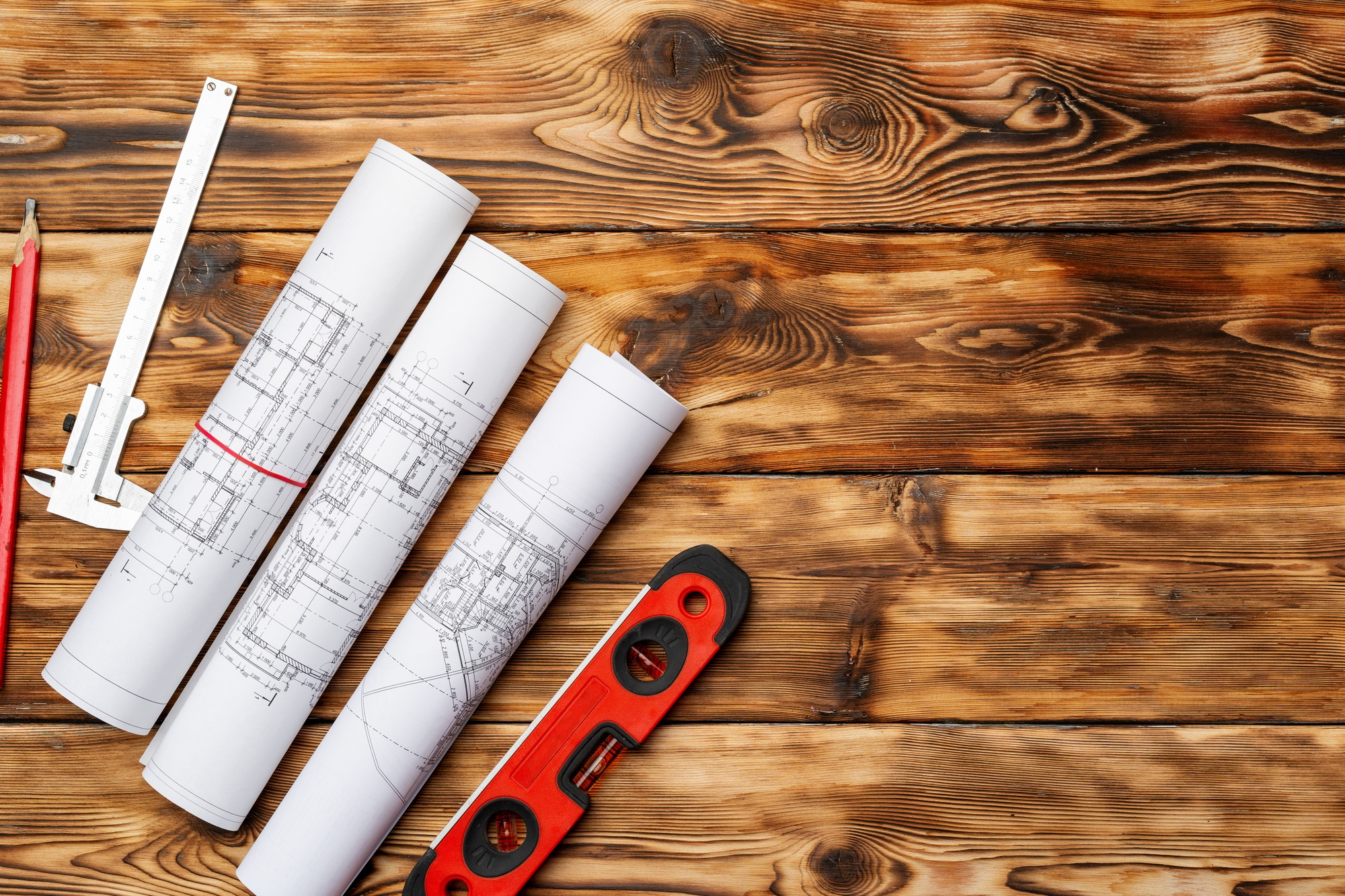 Rolled blueprints, level and ruler on wooden background