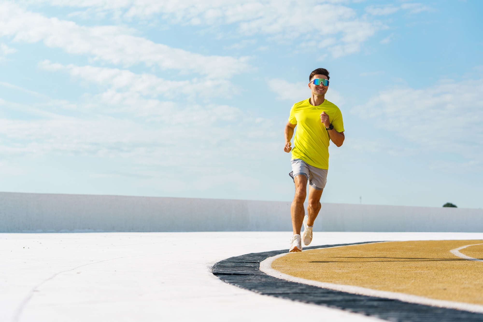 Runner in a bright yellow shirt on a curved track under a vibrant blue sky, exuding energy and focus