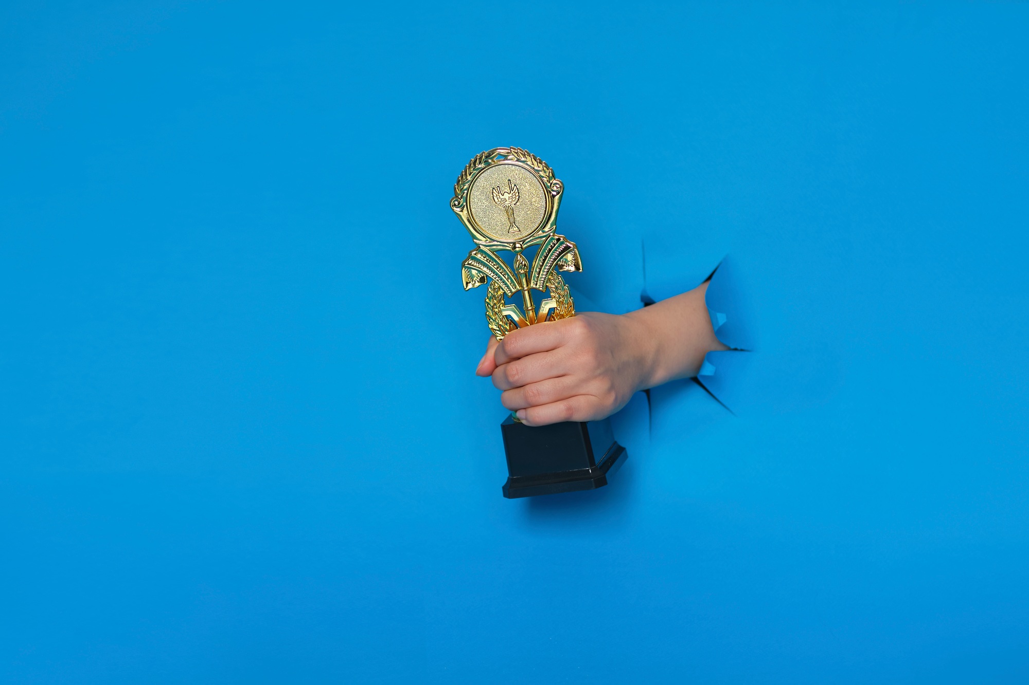 image of trophy in hand, concept for winning or success. Golden trophy on blue background, top view