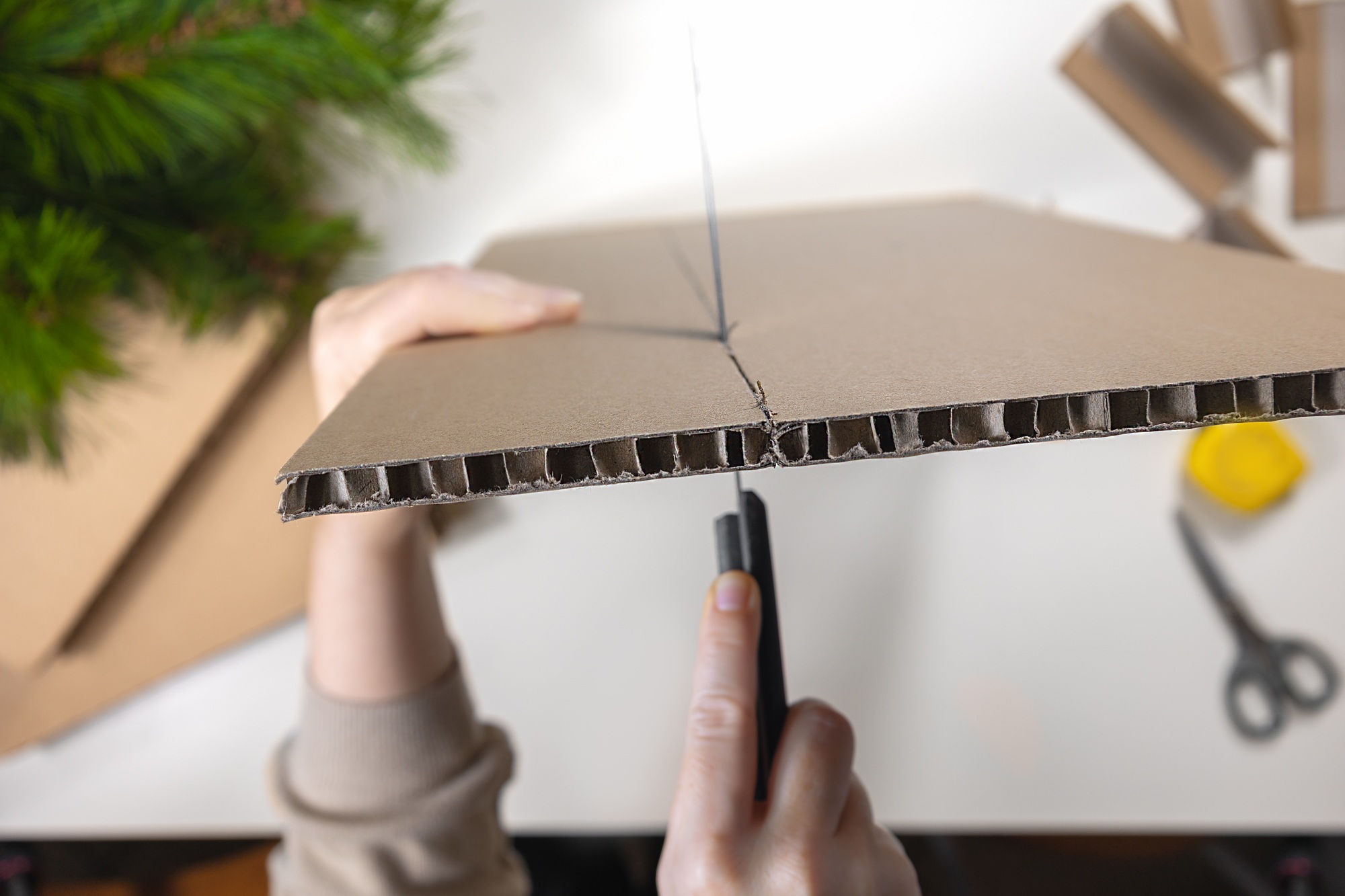 Selective focus close-up of a womans hands holding a knife cutting cardboard to make a coaster.