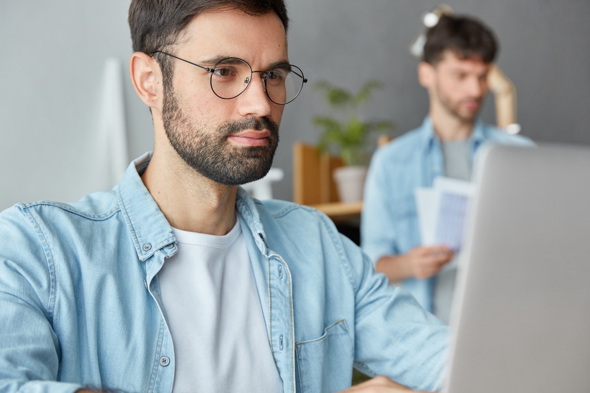 Serious bearded young prospective male entrepreneur makes business research on laptop computer, look