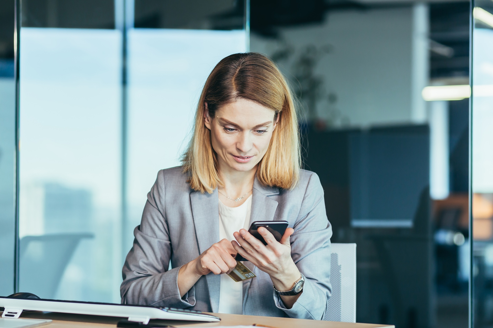 Serious business woman working in the office holding a phone, online choice, thinking