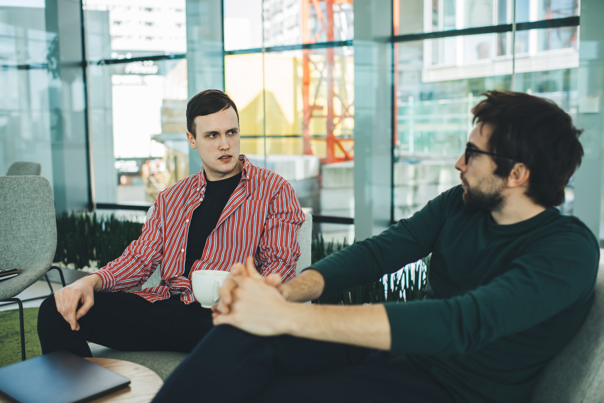 Serious young men discussing details of common project while sitting in modern office