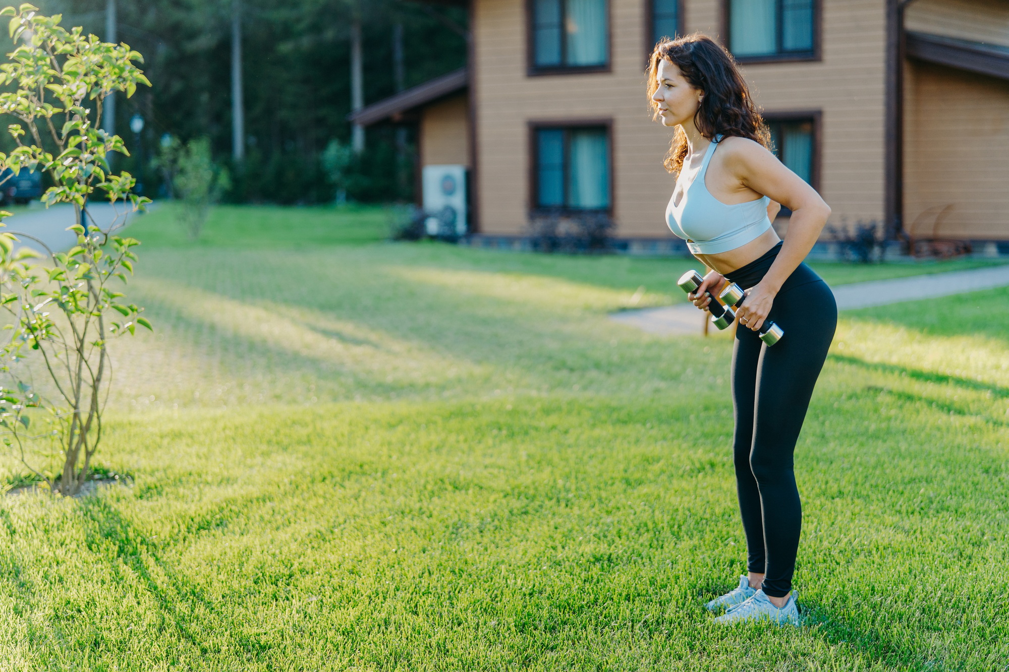 Shot of active sporty woman raises dumbbells and has workout session, works on biceps