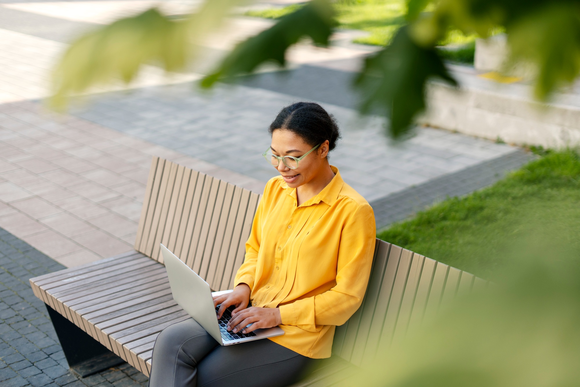 Smiling African American businesswoman using laptop computer working online, sitting on bench