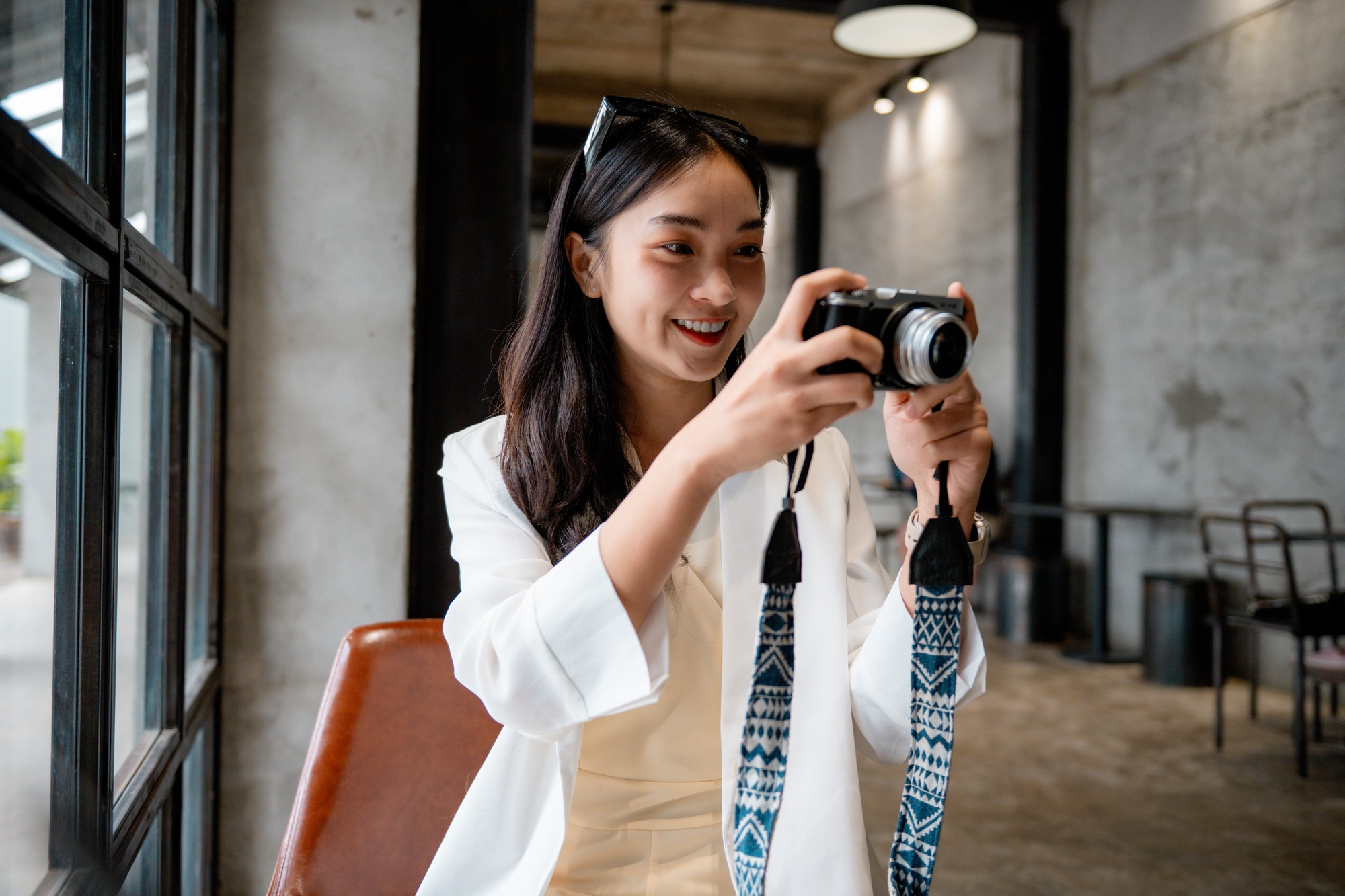 Smiling asian woman taking photos with a vintage film camera sitting in a coffee shop