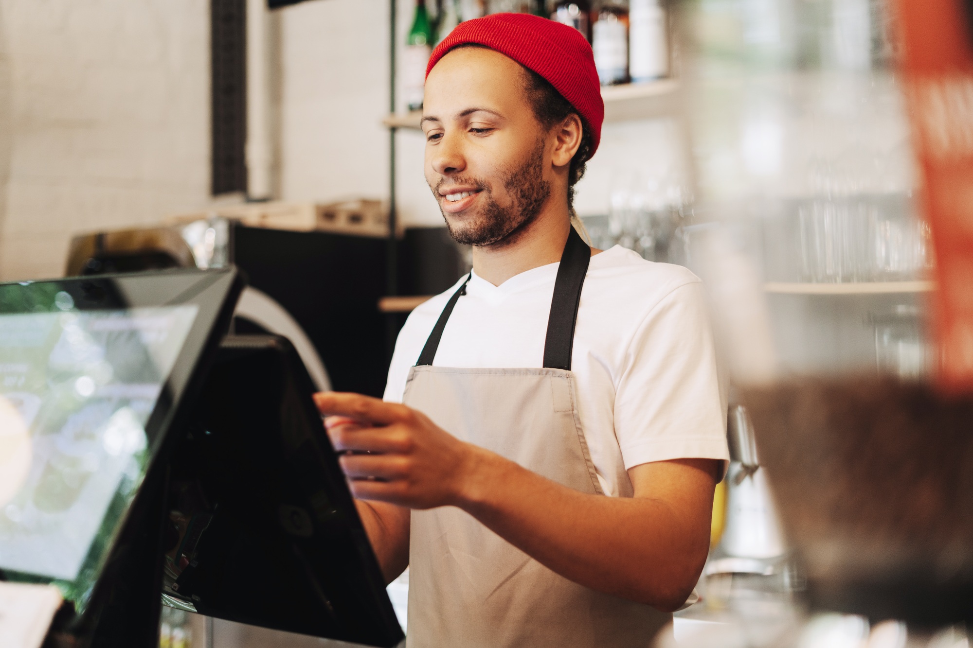 Smiling barista, Latin man in red hat taking order on digital pos system