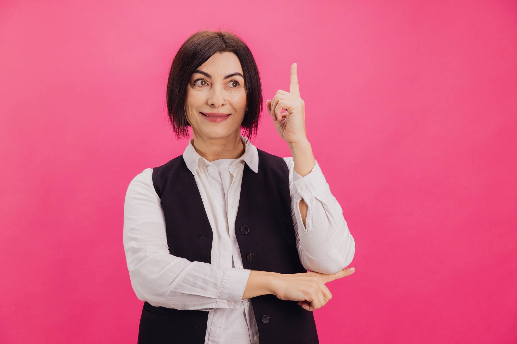 Smiling businesswoman having an idea pointing finger up on pink background