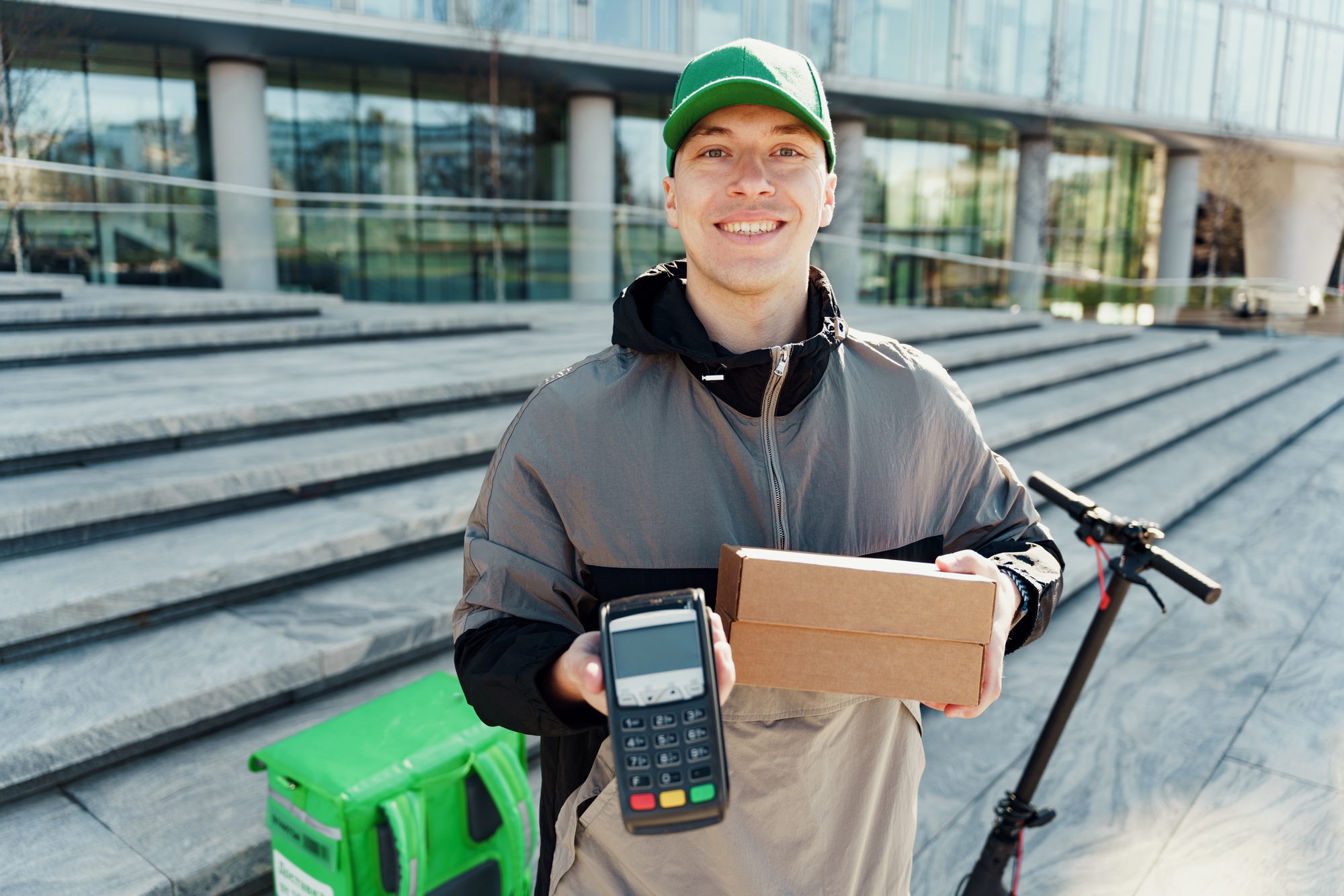 Smiling delivery man with package and POS machine outdoors.