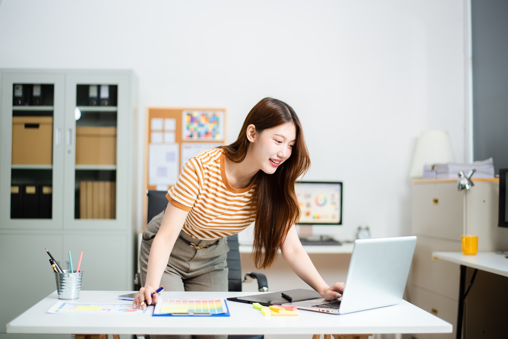 Smiling designer working on colorful branding and chart plans at desk with laptop