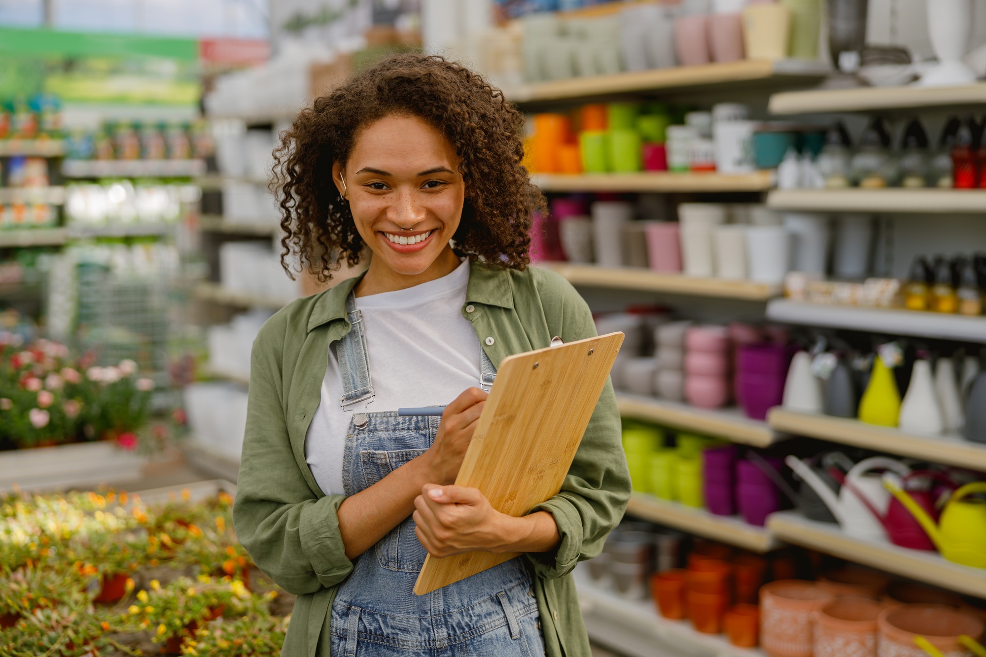 Smiling woman florist with clipboard conducts inventory in flower garden center