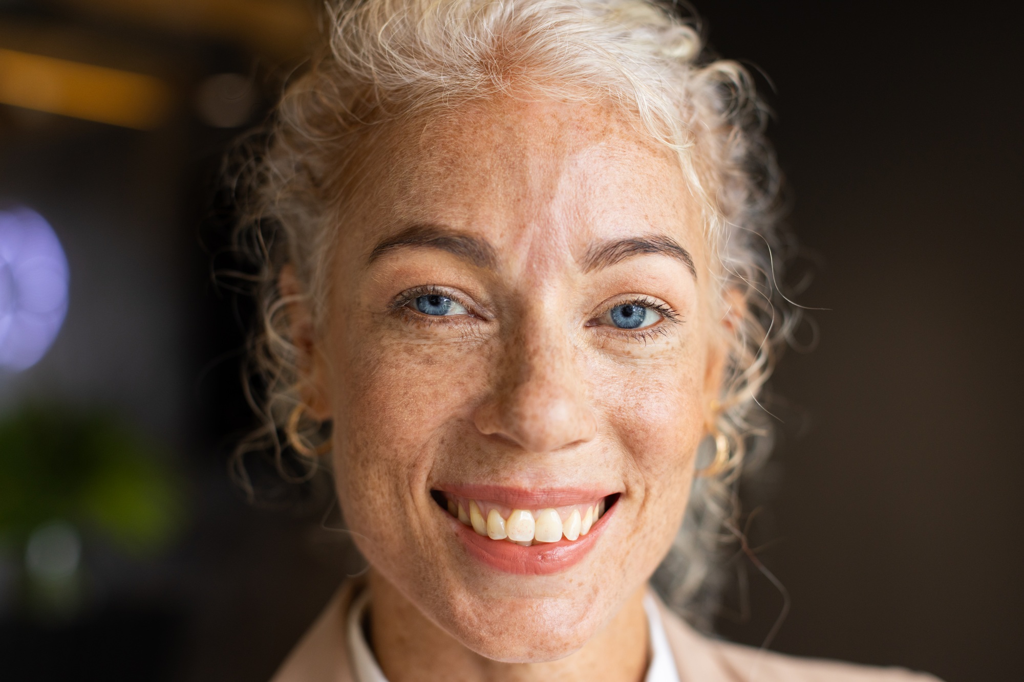 Smiling woman with curly hair and freckles, close-up portrait in office setting