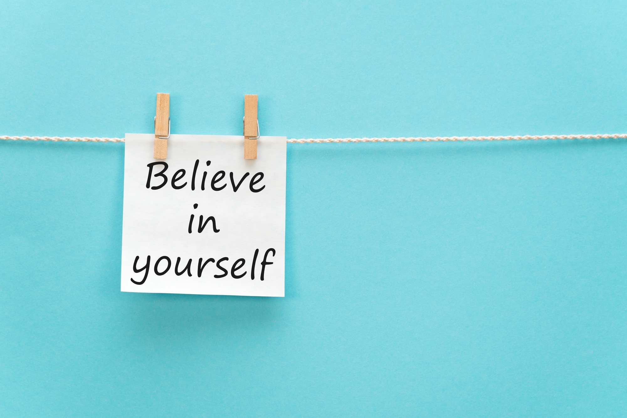sticker with the inscription believe in yourself hangs with a clothespin on a rope on a blue back