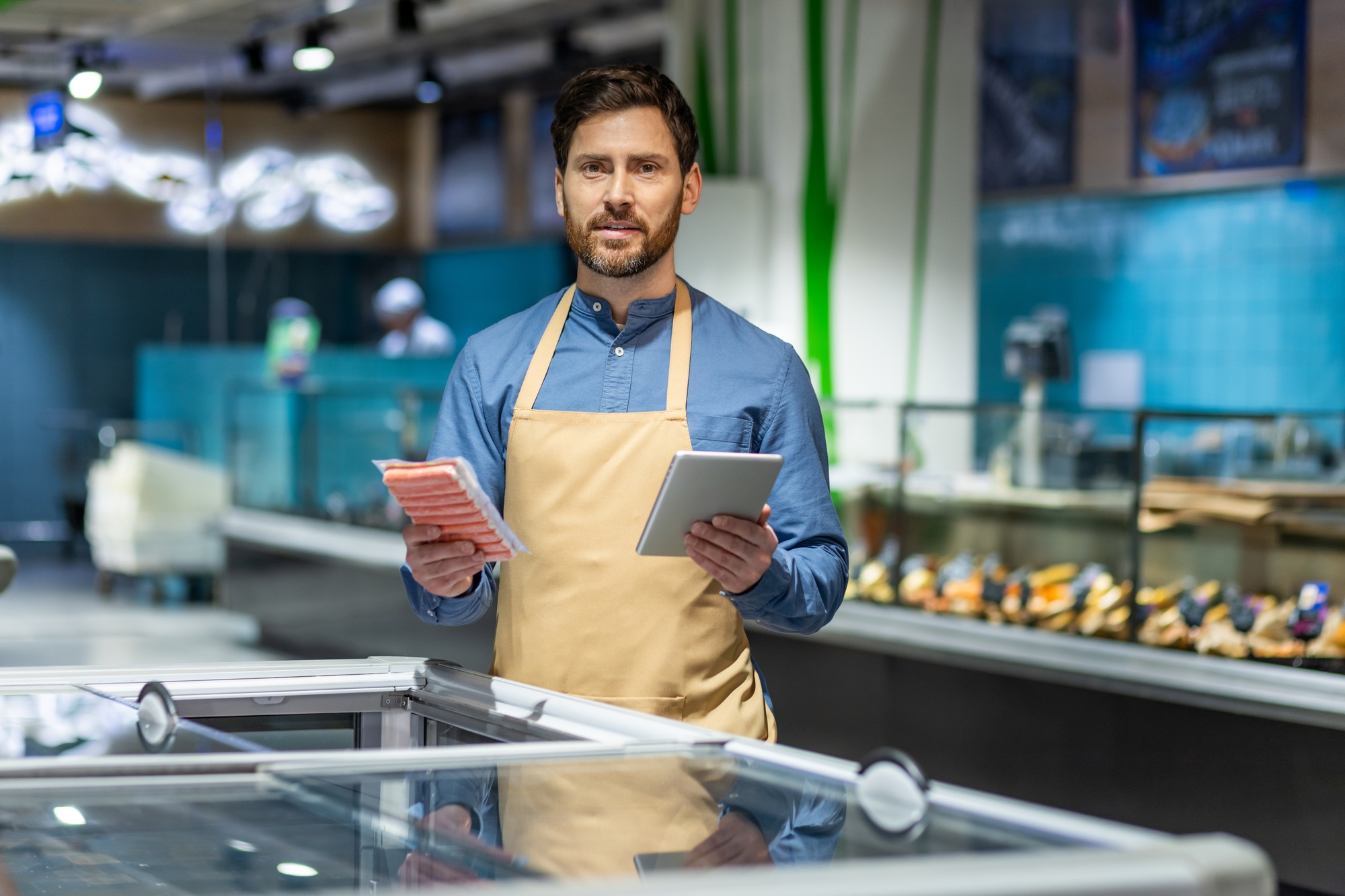 Store clerk holding tablet and packaged meat in grocery store, showcasing inventory management in