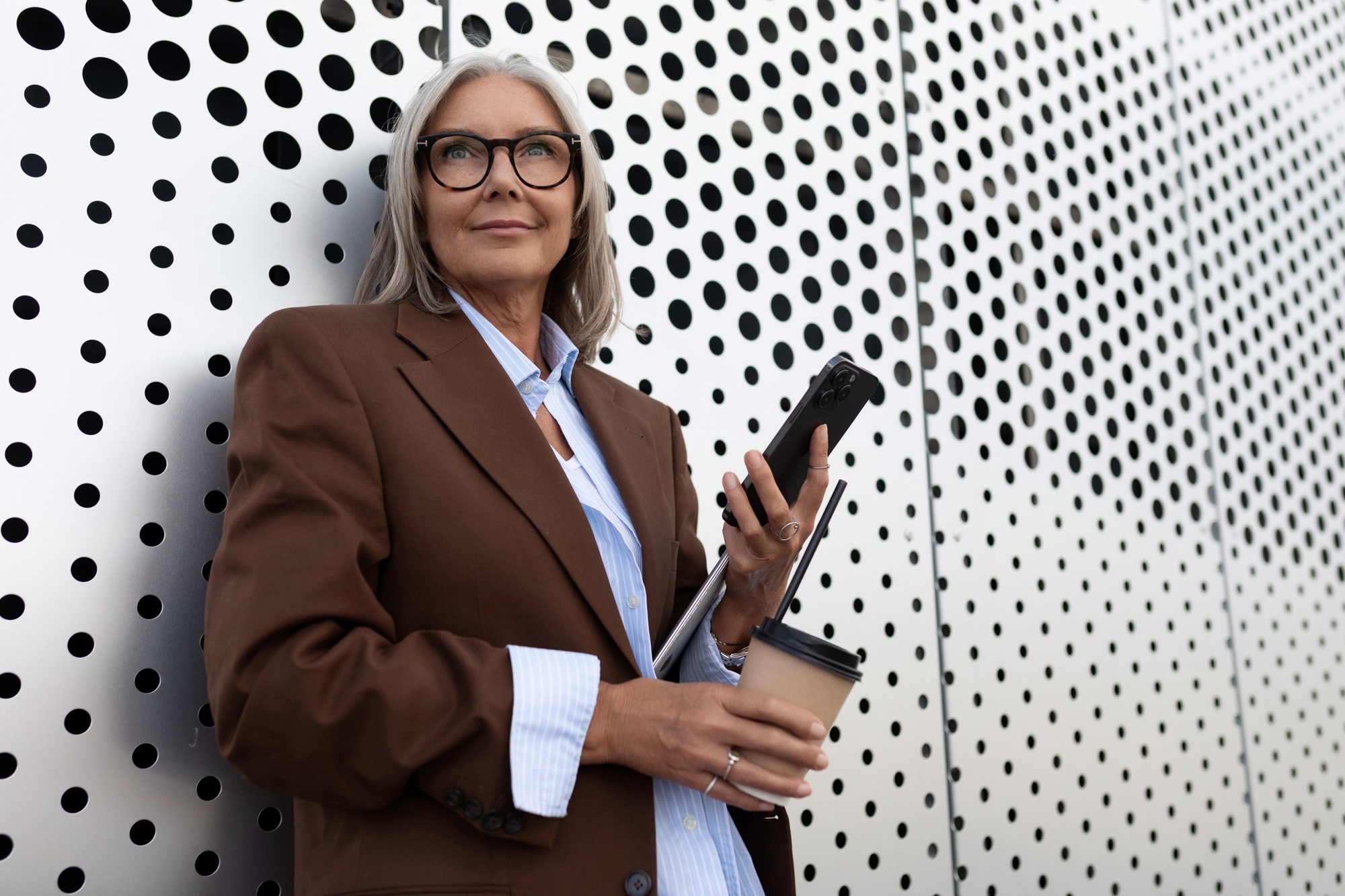 successful gray-haired business grandmother dressed stylishly uses a smartphone while walking along