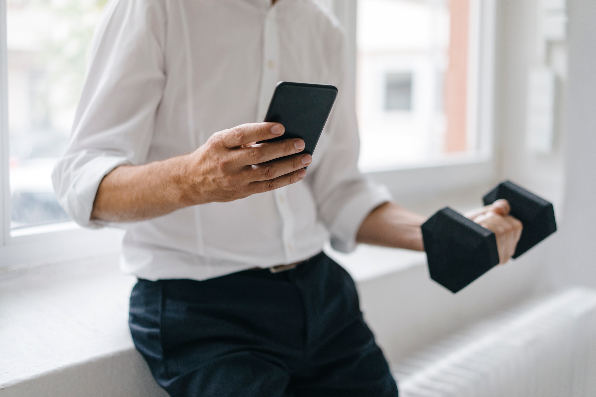 Successful manager using smartphone and training with a dumbbell