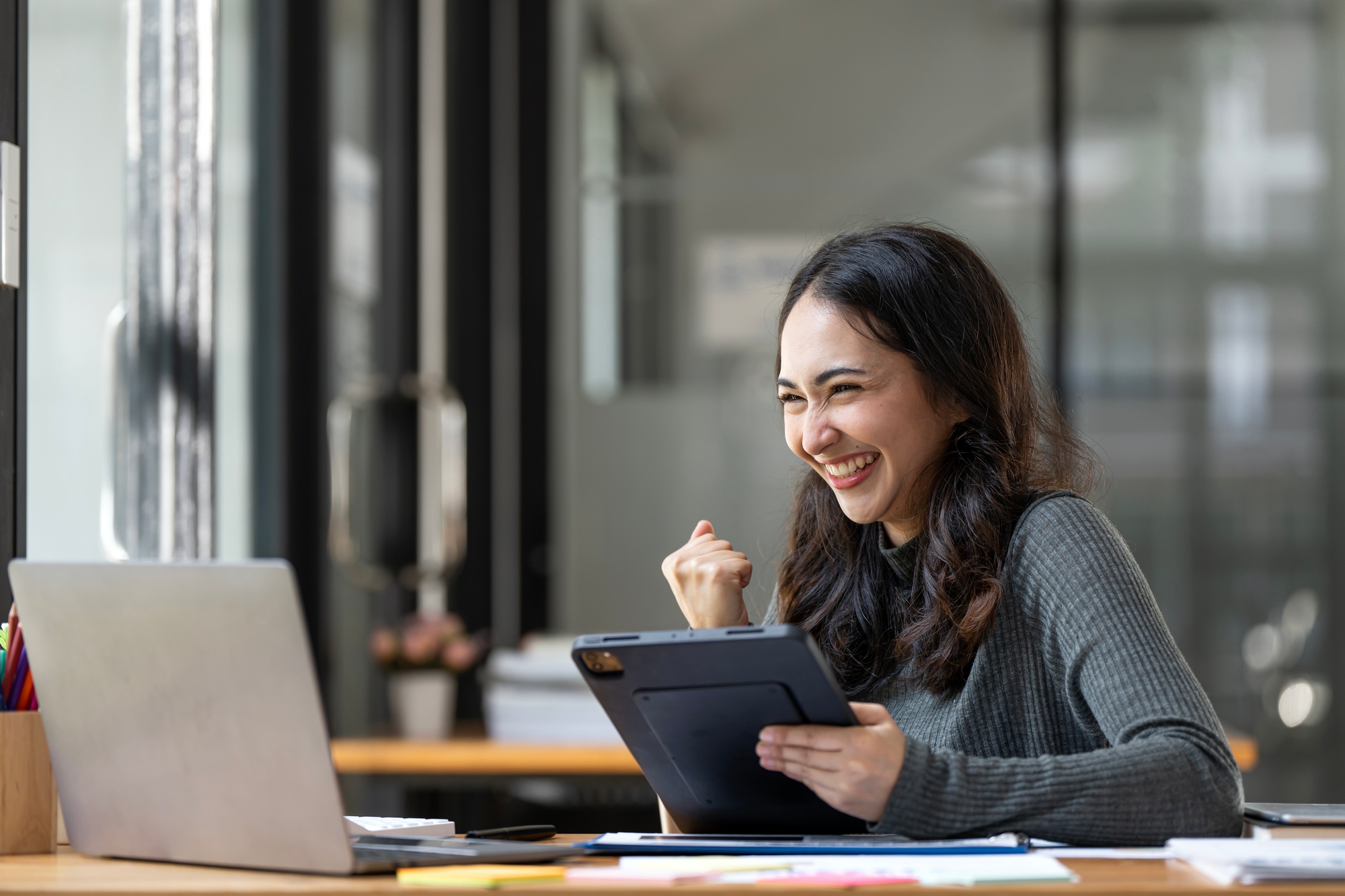 Successful young Asian business woman achieving goals excited  with laptop in the office.