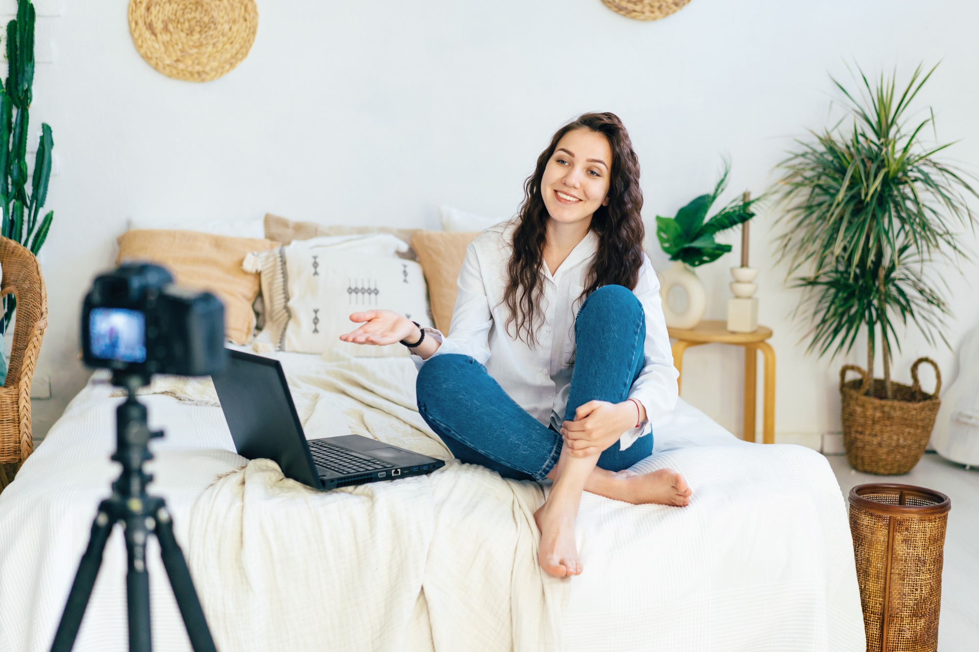 The blogger girl sits on the bed in the bedroom and records a video clip on the camera.