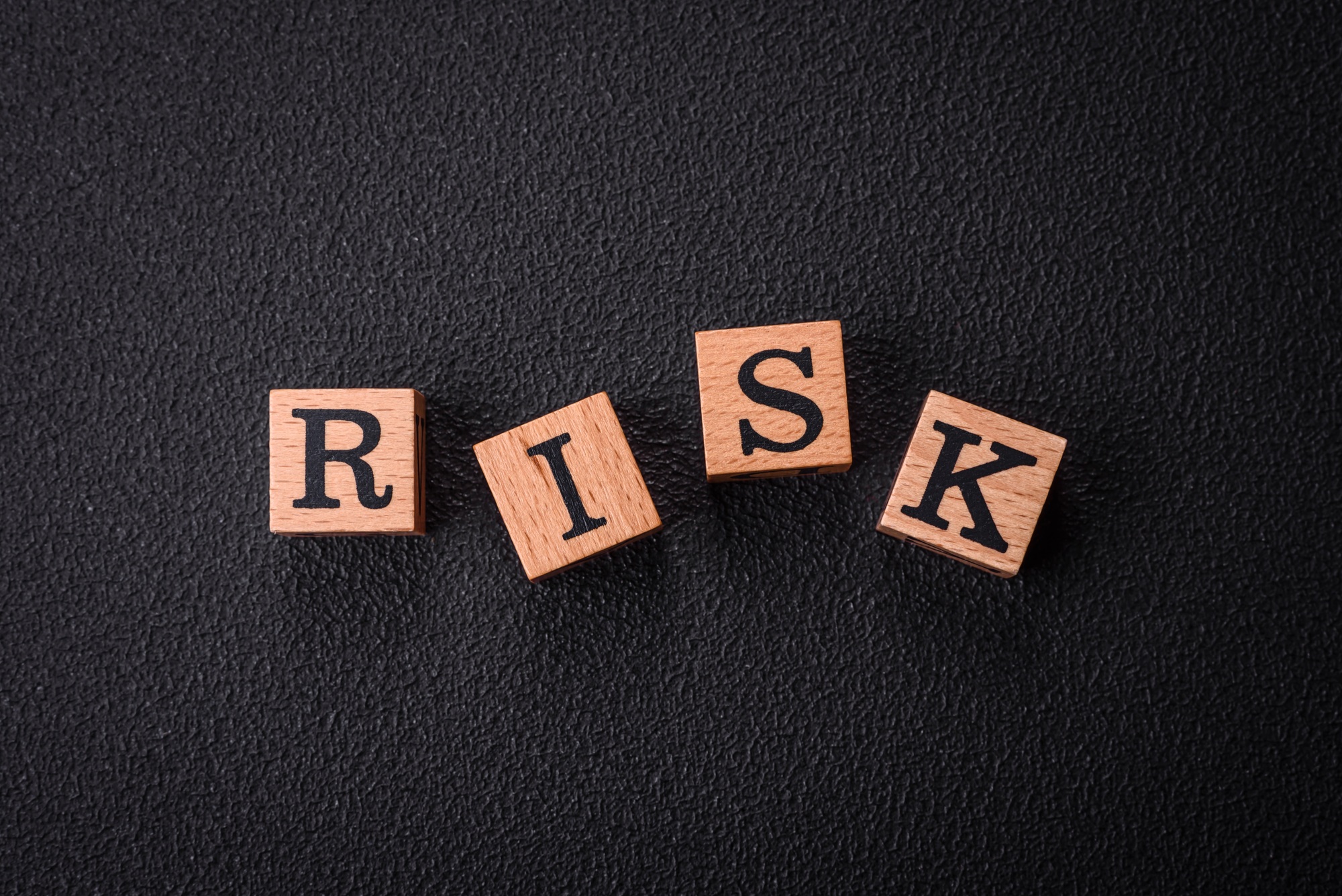 The inscription risk with wooden cubes on a dark concrete background