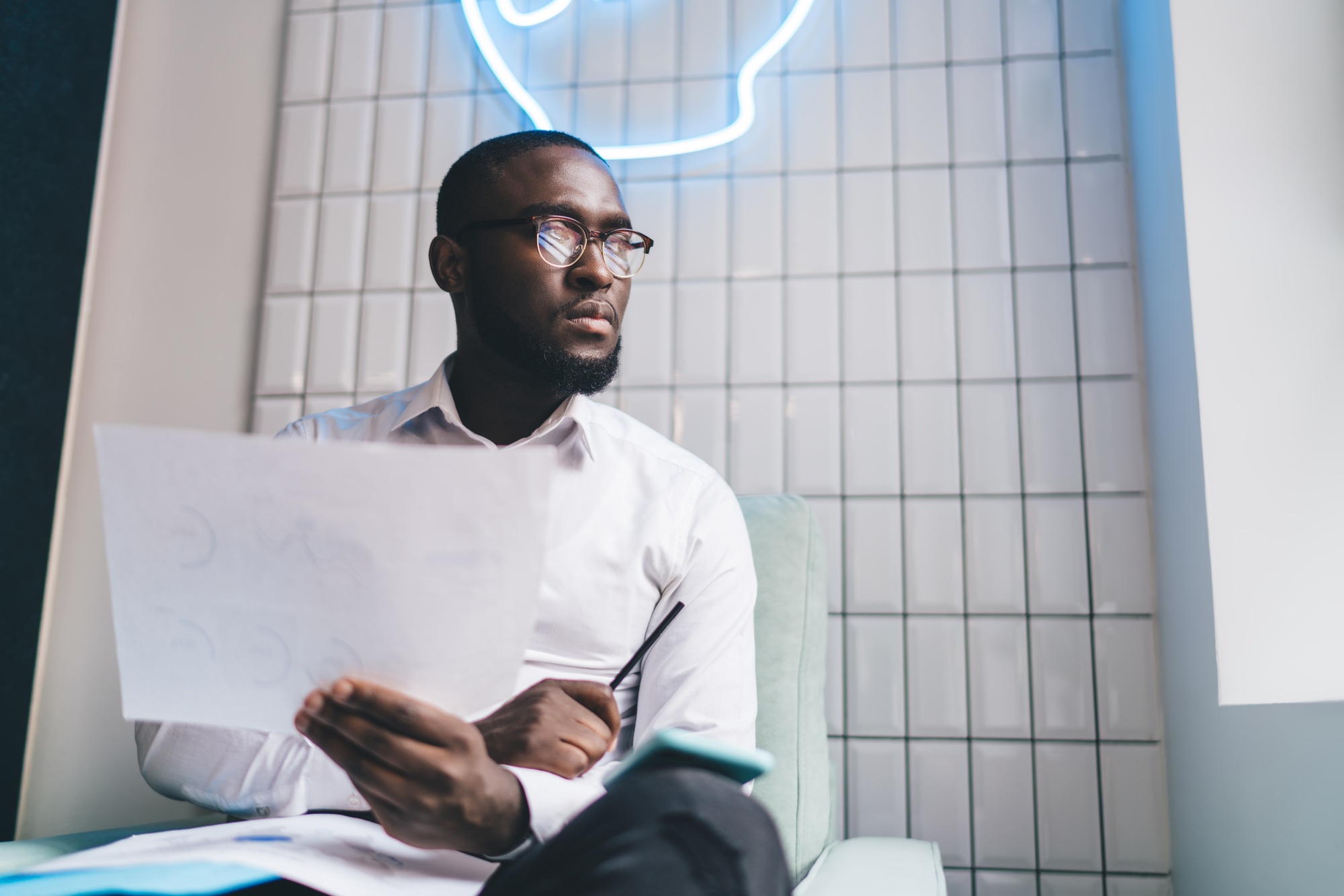 Thoughtful black man with document looking away in office