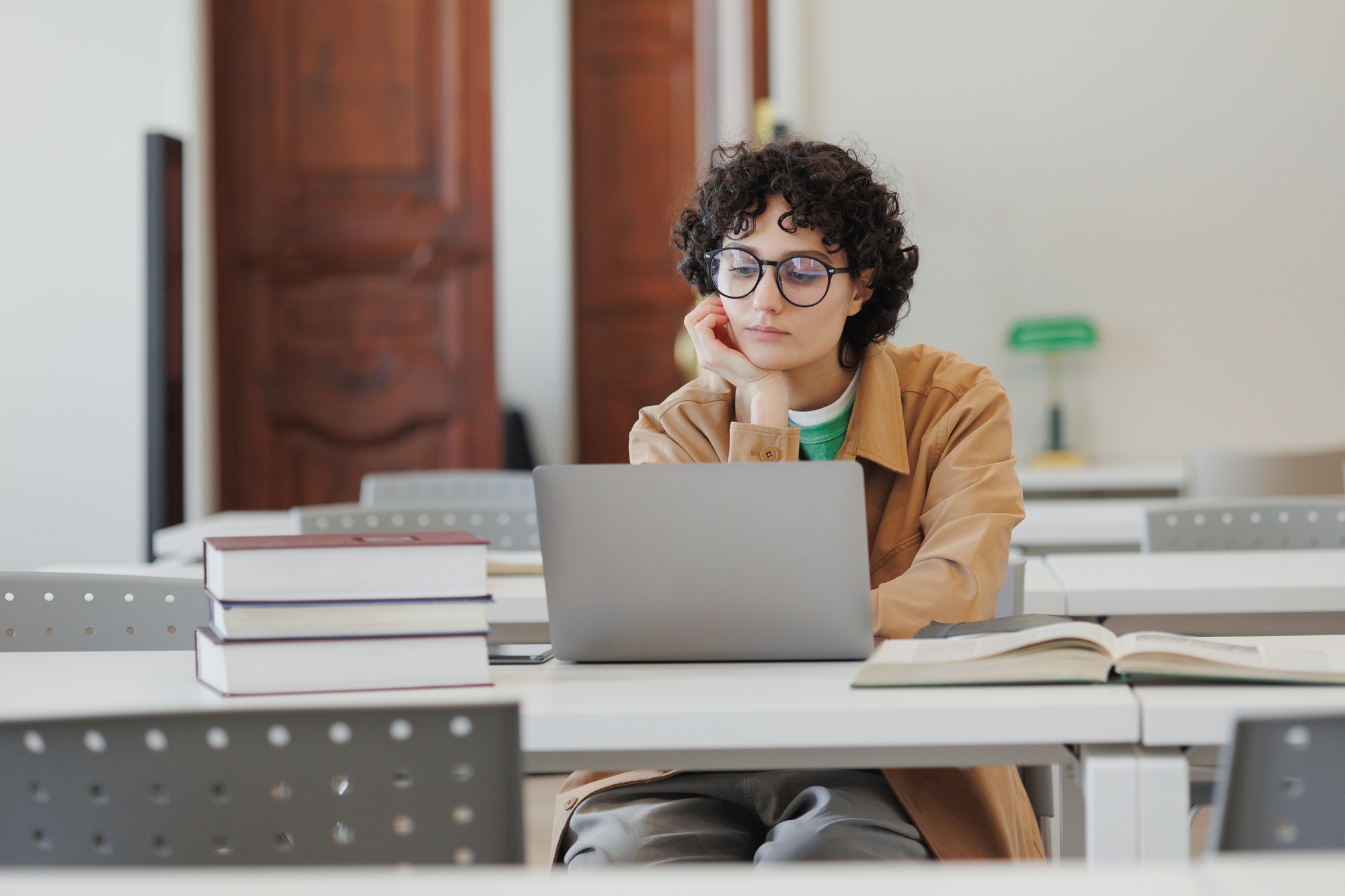 thoughtful woman in library, watches online training webinar and takes notes in notebook.