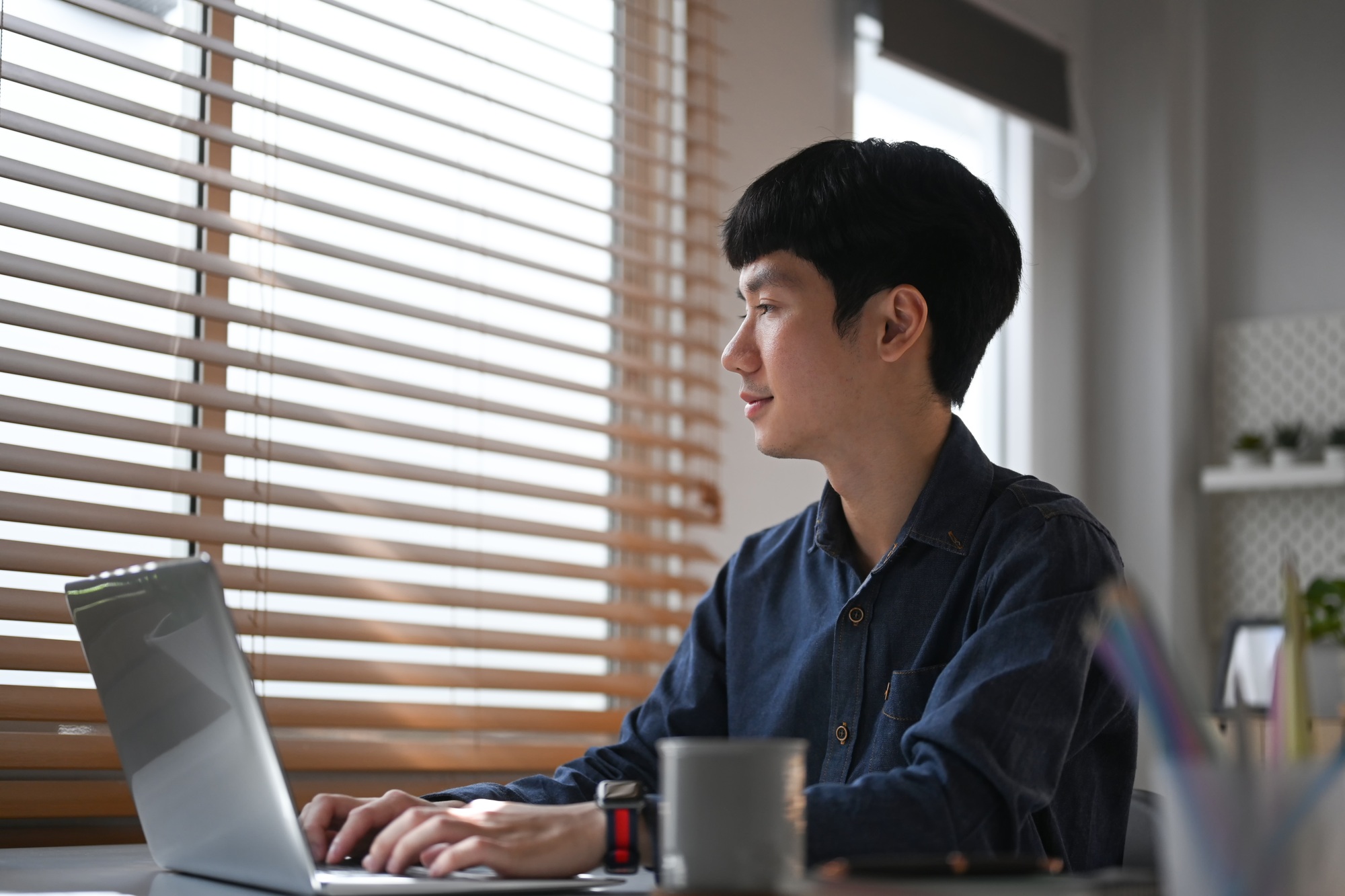 Thoughtful young businessman typing business email, working with laptop at comfortable home office.