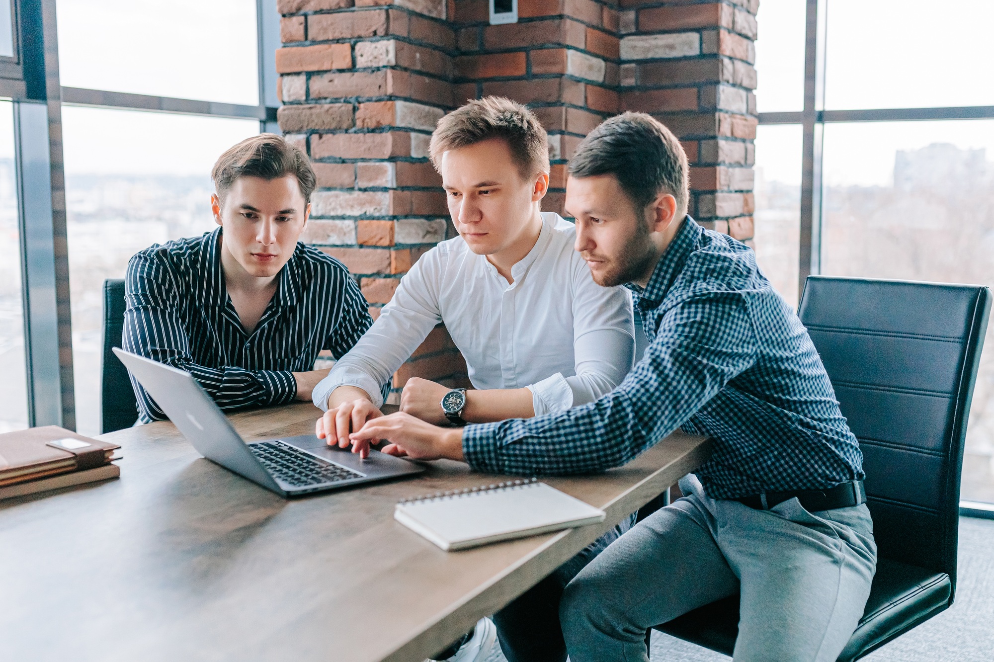 Three guys working on their laptops, with a trainer providing support and feedback
