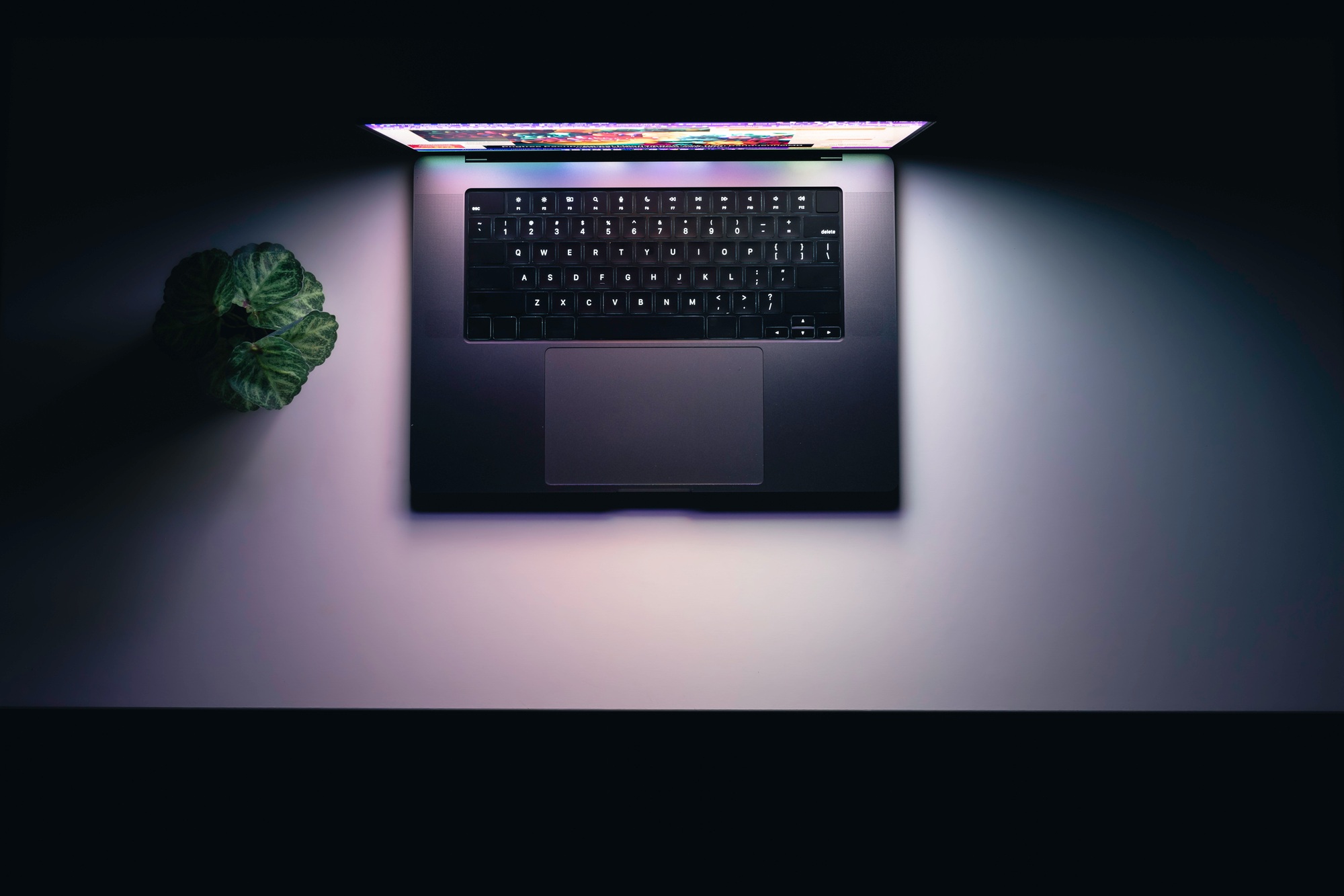 Top view of a laptop on a table, glowing screen in the dark.