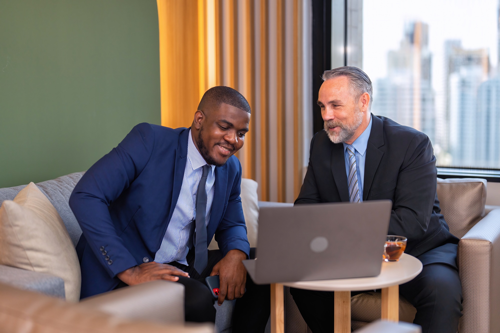 Two businessmen sitting on sofa working discuss on financial forecast together on laptop information