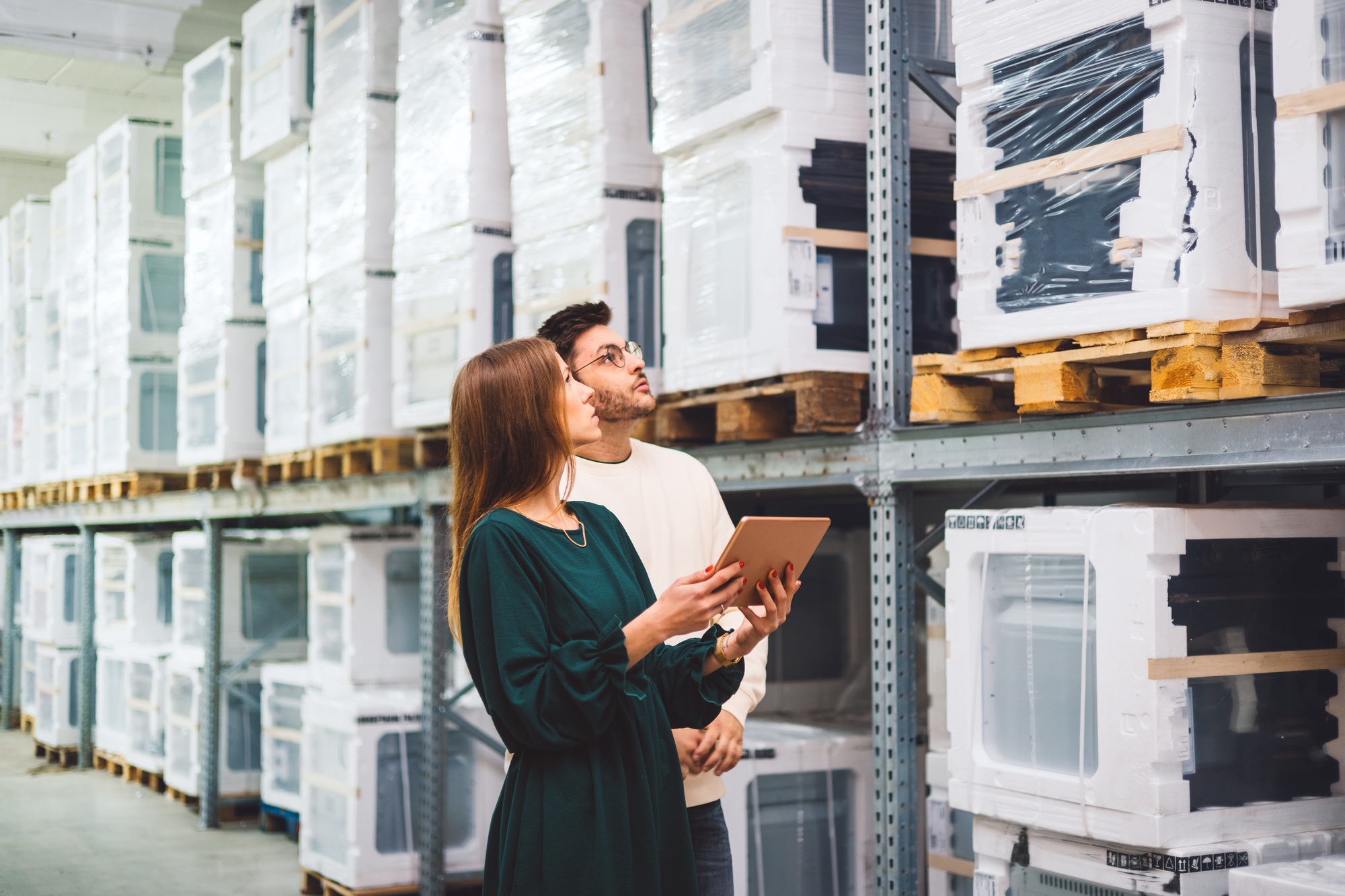 Two warehouse workers checking warehouse inventory management system, items in stock.