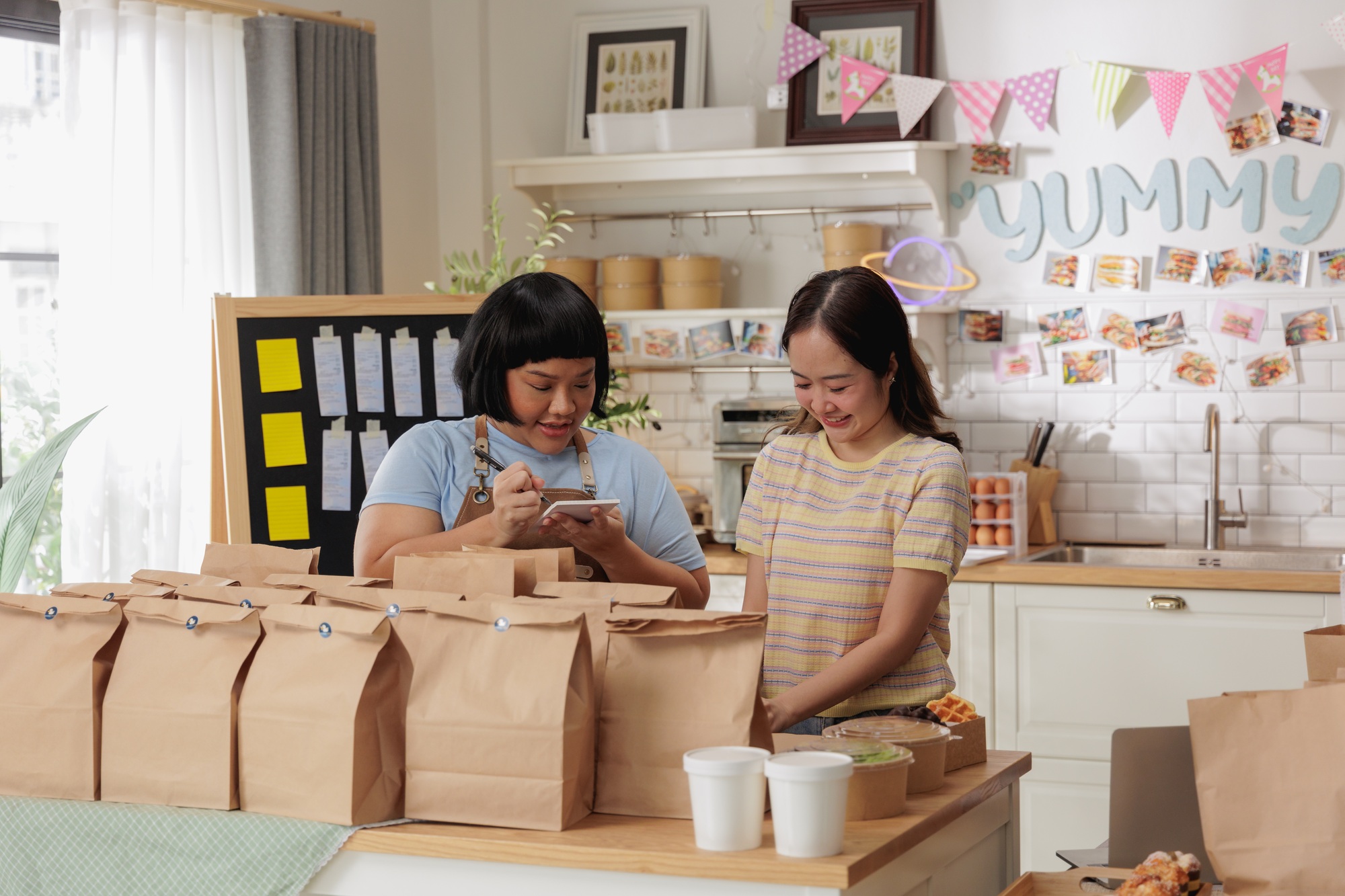 Two women packing food orders in a bright kitchen, celebrating a small home-based business
