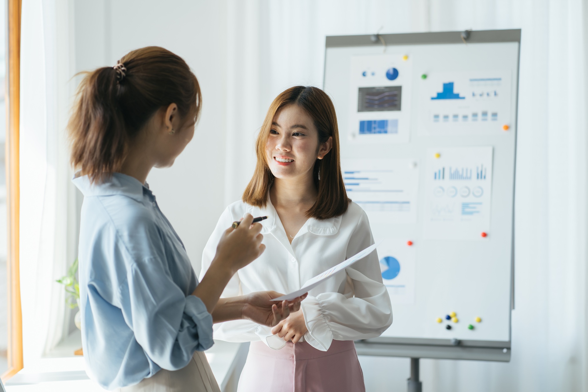 Two young businesswomen doing a presentation in a meeting or conference standing in front of a flip