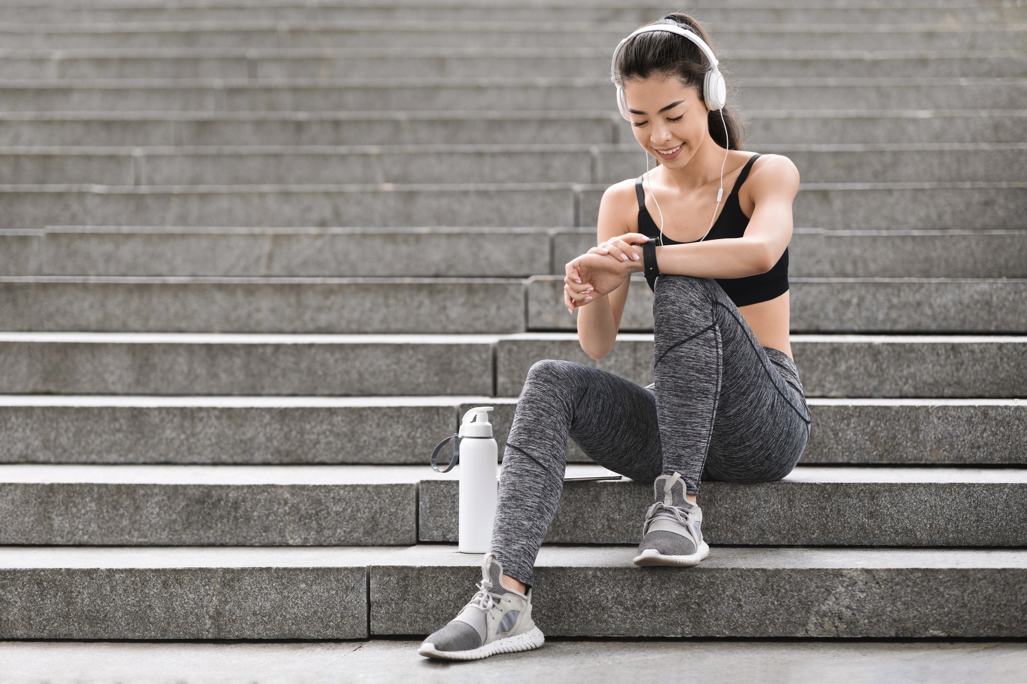Urban Sport Concept. Smiling Asian Girl Checking Smartwatch Settings Before Jogging Outdoors