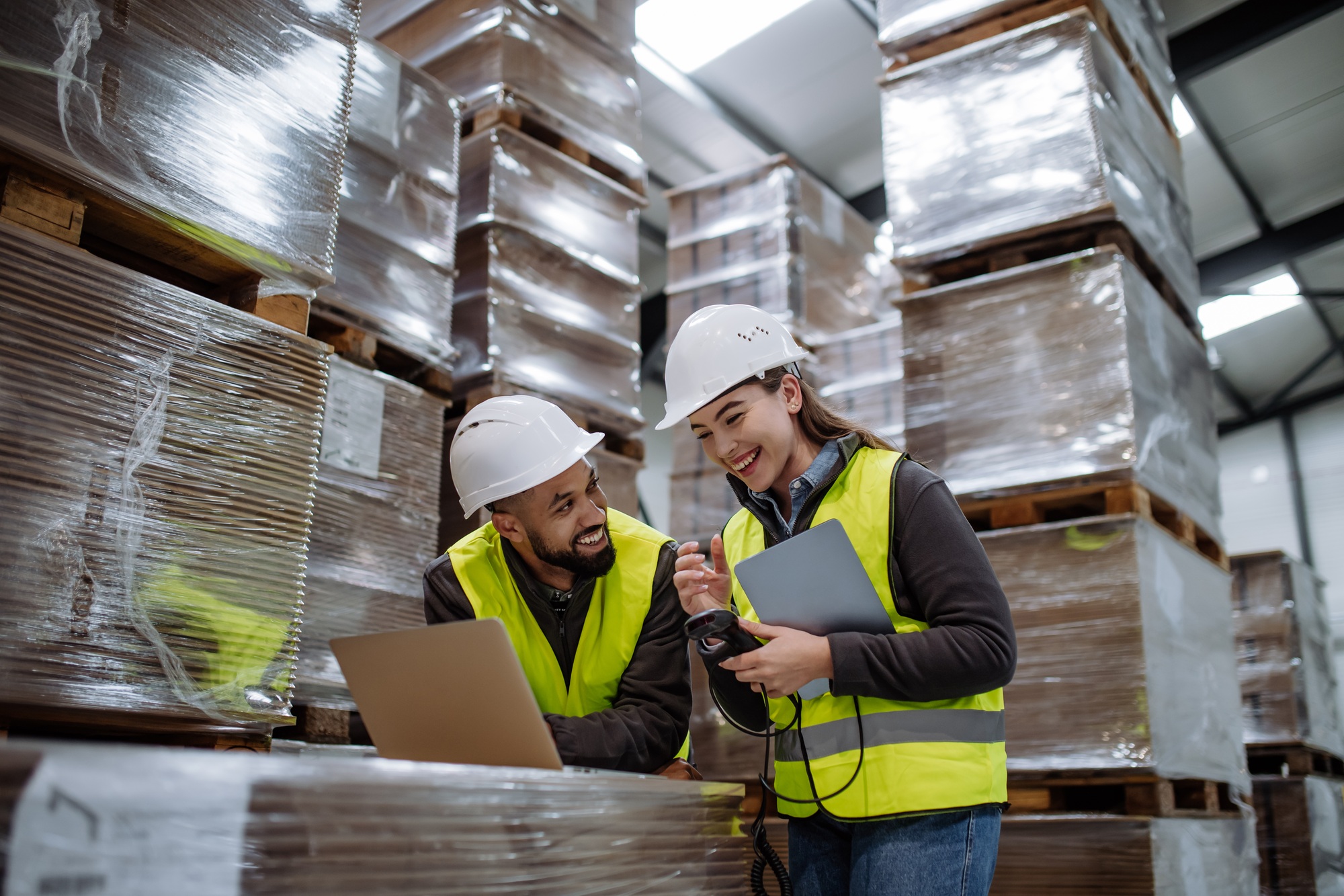 Warehouse manager talking and laughing with logistics employee in warehouse, planning transport of
