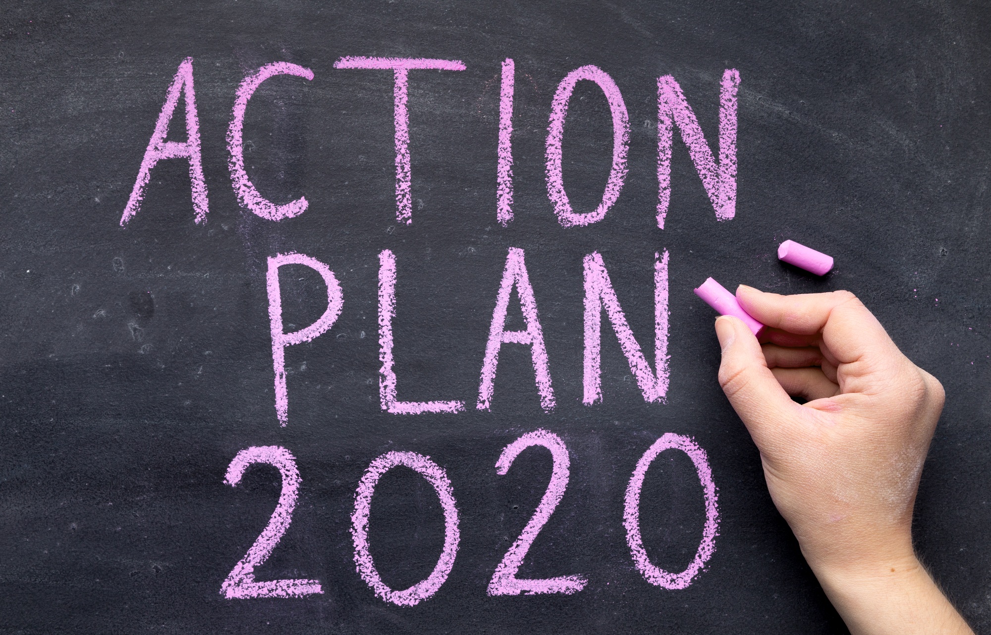 Woman hand writing action plan with chalk on black board