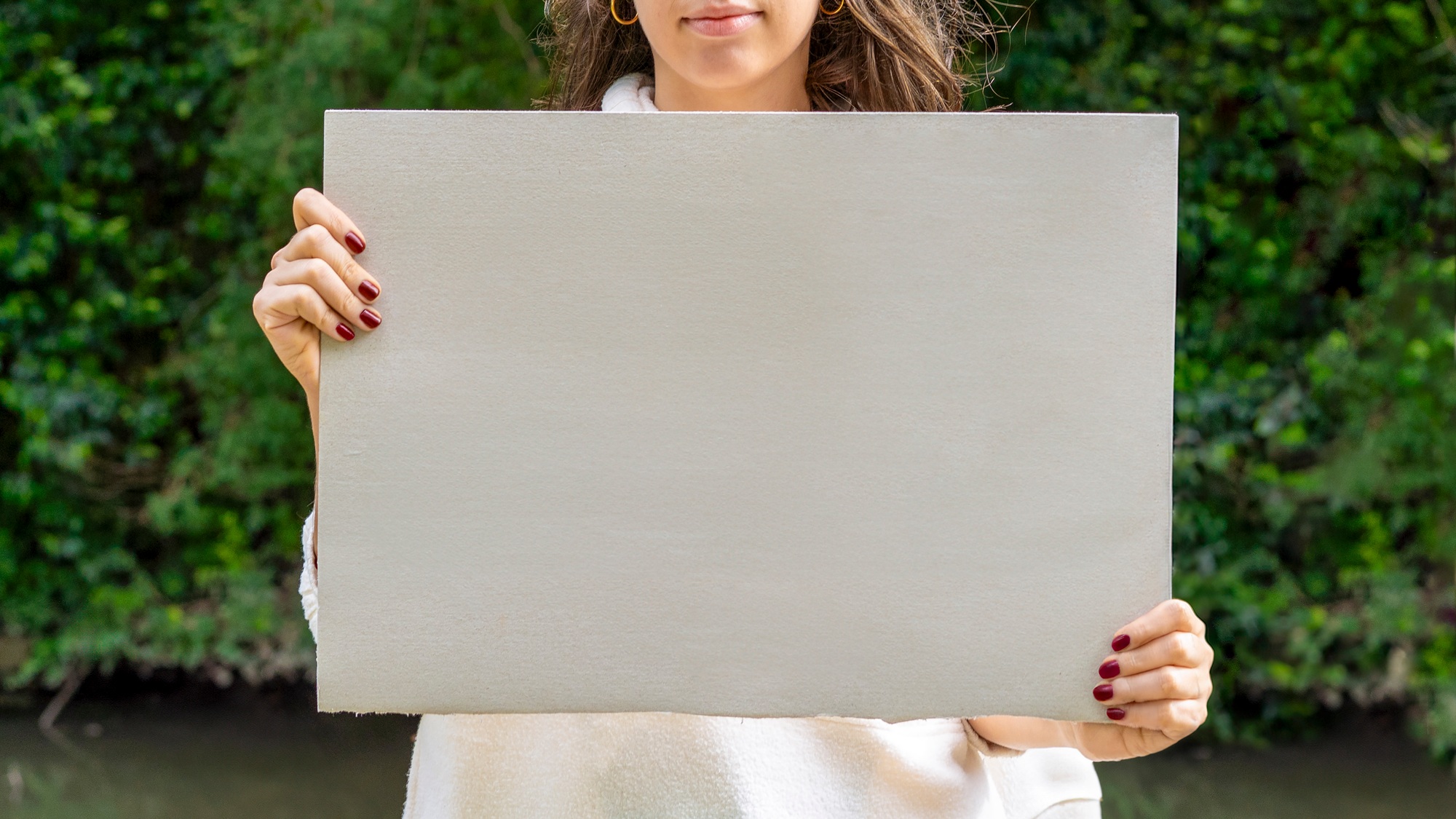 Woman holding a blank sign by the river, ready for a message