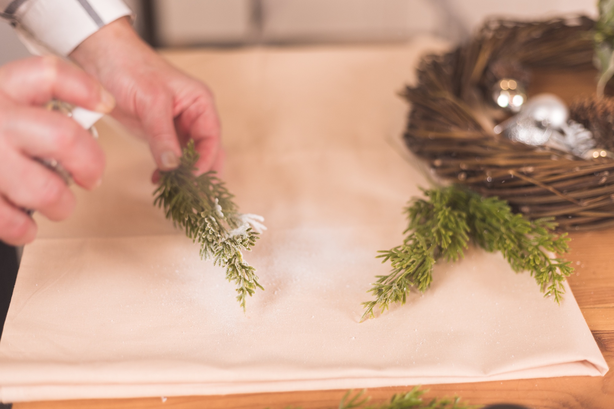 Woman needleworker spray artificial snow on a fir branch doing handmade wreath for Christmas