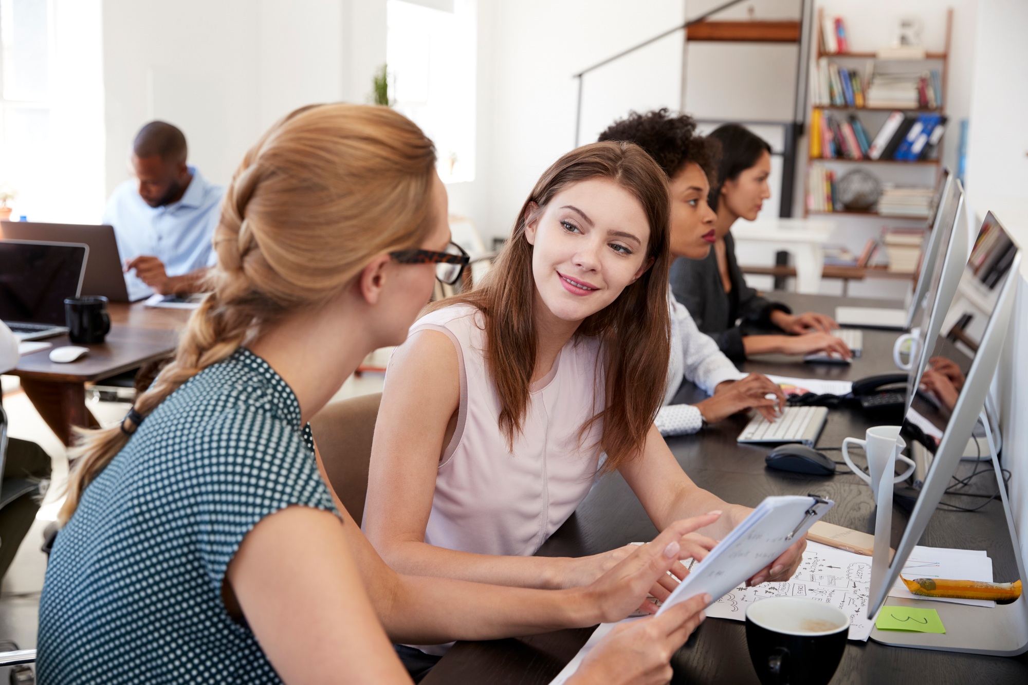 Woman training new female employee in an open plan office
