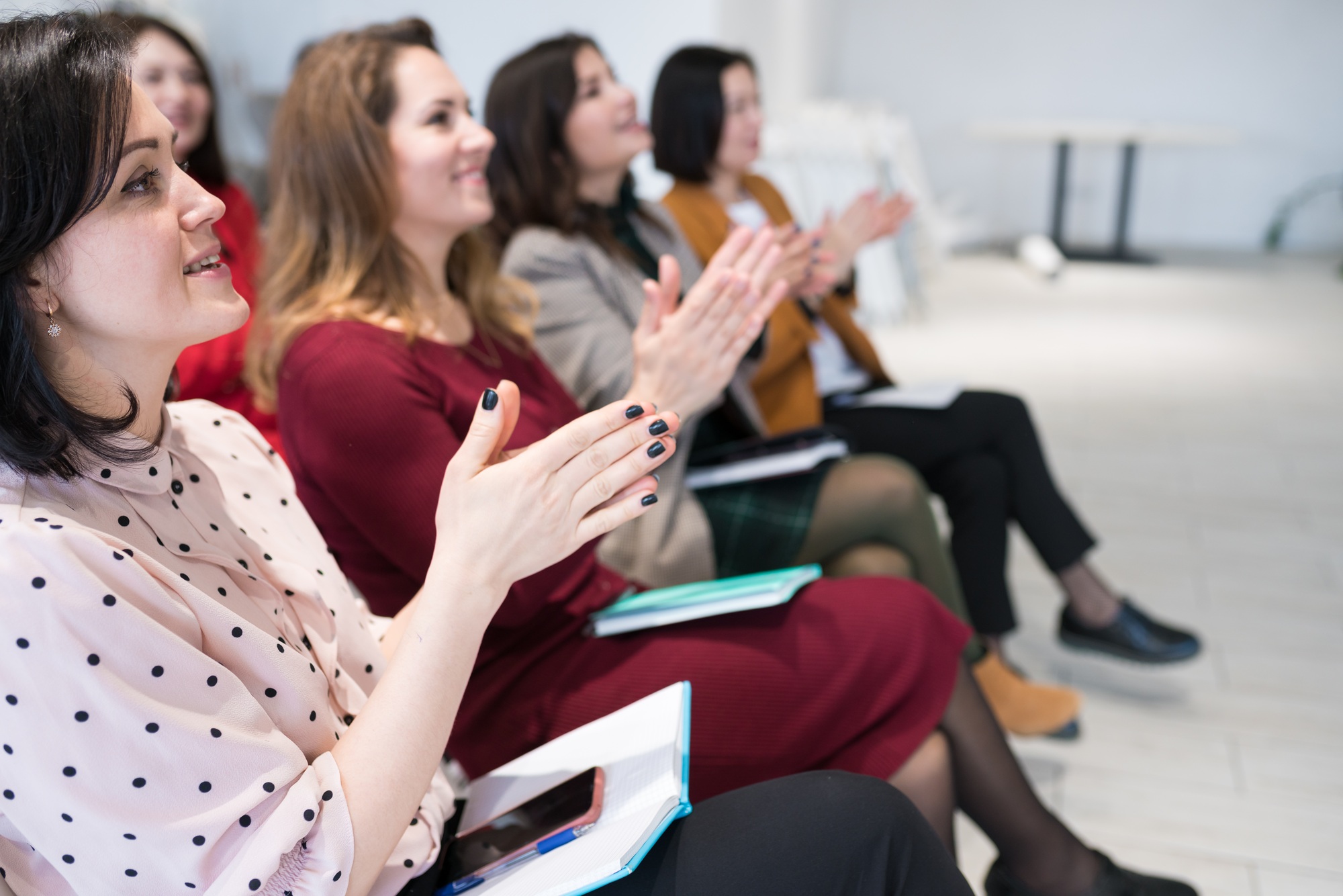 Women applauding speaker at group session, sitting in audience at training meeting