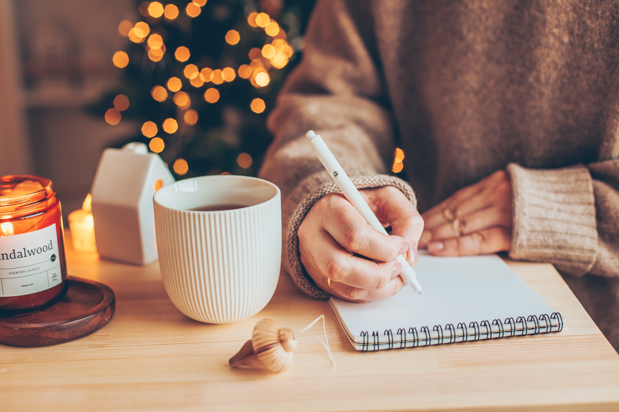 Women writing goals and plans in notebook, drinking a mug with tea or coffee, burning candle