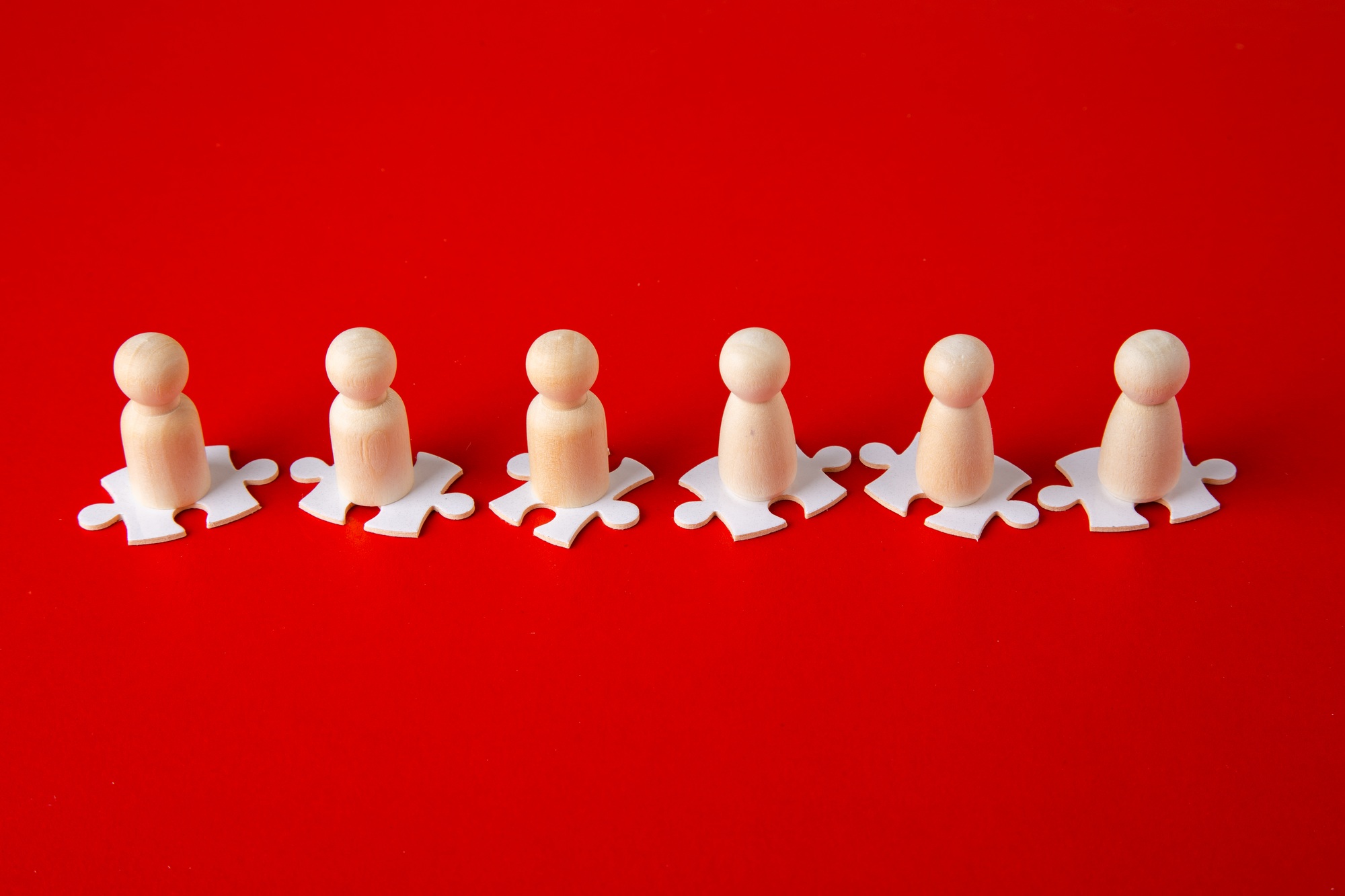 Wooden figures on puzzles on red background as a symbol of team building.