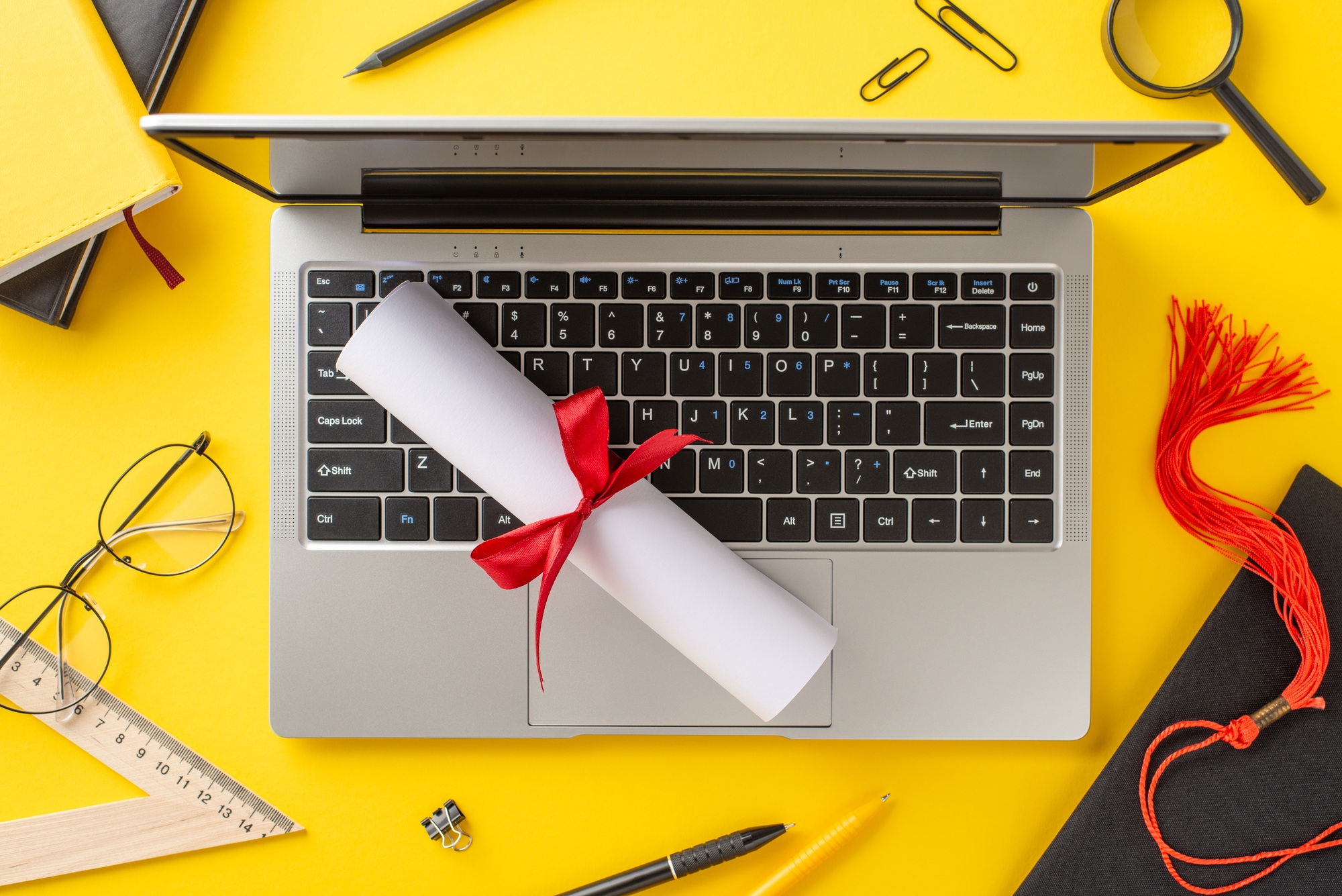 Yellow background shows a laptop with a rolled diploma tied with red ribbon
