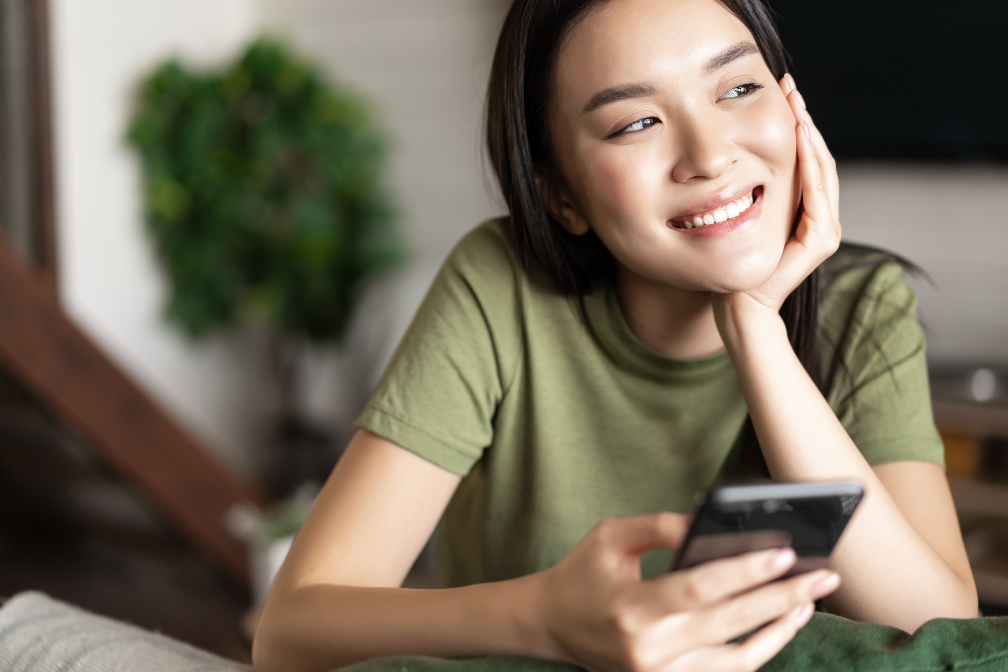 Young asian woman placing an order, waiting for delivery on mobile phone app, sitting at home and