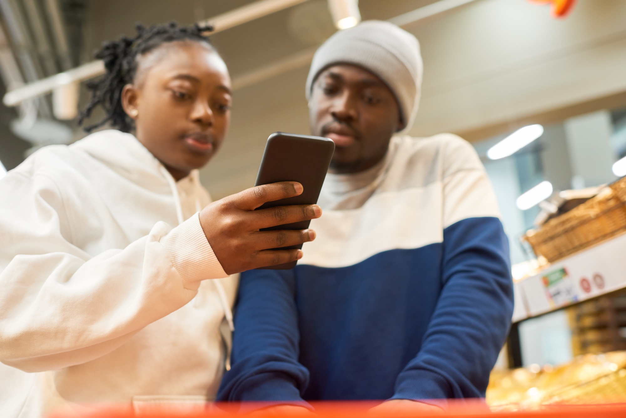 Young black woman with smartphone showing shopping list to her boyfriend