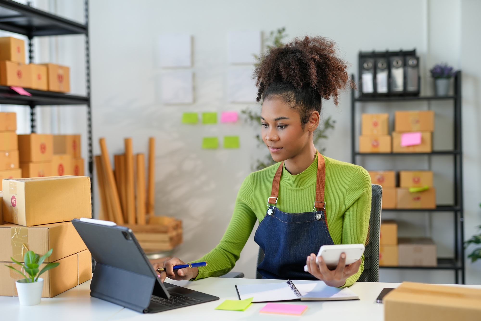 Young entrepreneur calculating costs of her business using tablet and calculator
