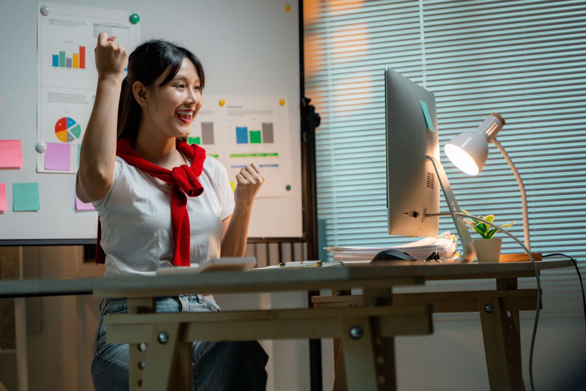 Young entrepreneur feeling happy about achieving business goals, raising arms in front of computer