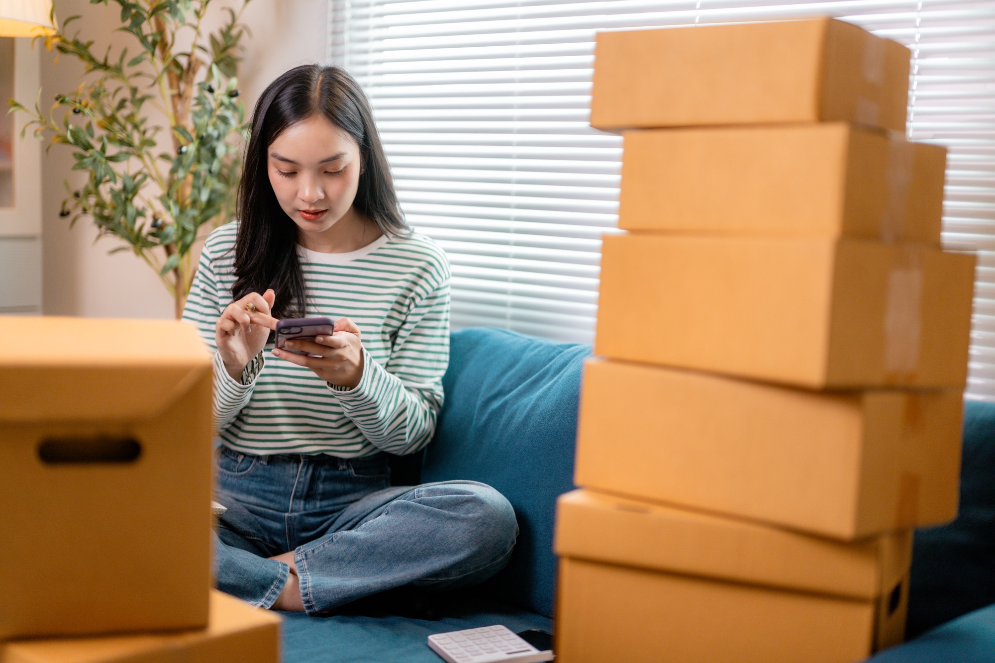 Young entrepreneur managing online sales using smartphone and cardboard boxes